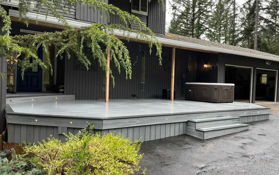 Gray deck with a hot tub outside a dark gray house with a garage.
