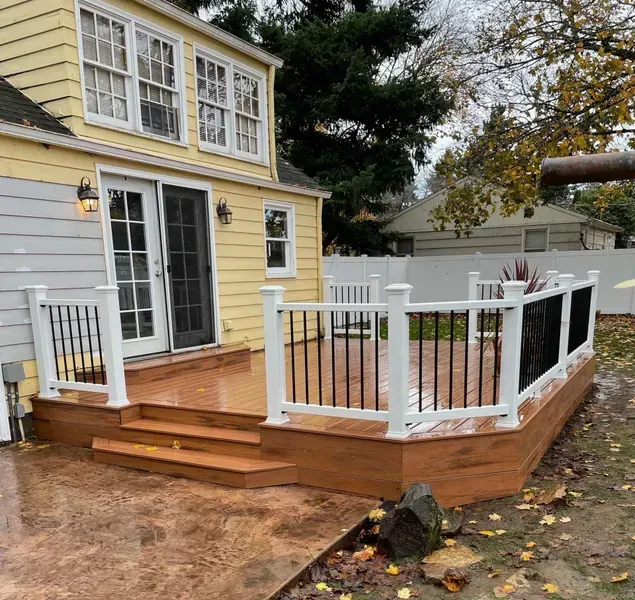 Backyard deck with stairs, black iron railings, and white posts. House in background is yellow.