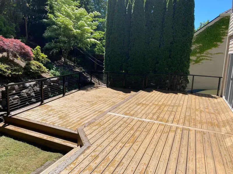 Wooden deck with steps, black metal railing, and a tall evergreen hedge.