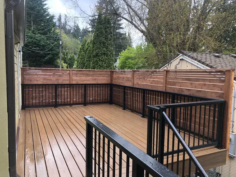 Wooden deck with black railings and a wood-slat privacy fence, surrounded by trees.
