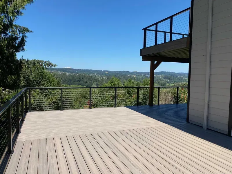 Large wooden deck with cable railings and expansive view of green valley and blue sky.