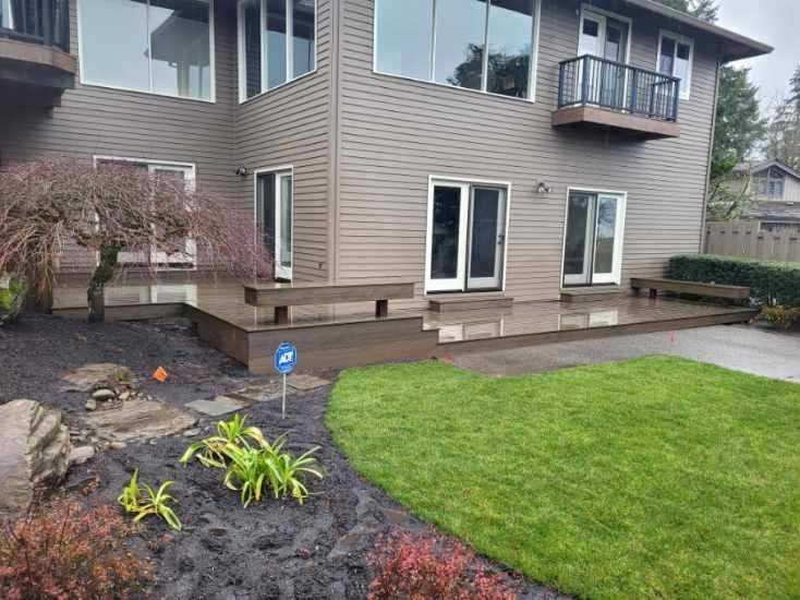 Back of a house with a brown deck, glass doors, and a green lawn.