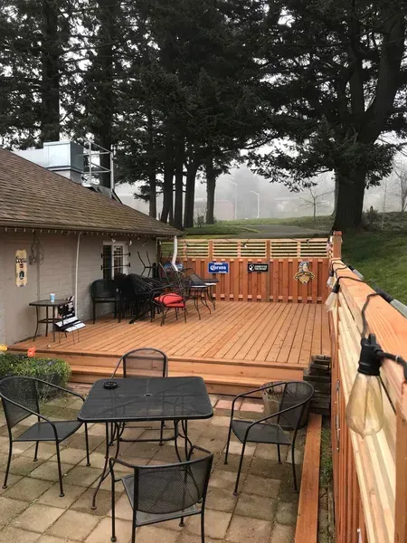 Wooden deck with patio furniture, attached to a house. Wooden fence on the right. Trees in the background.