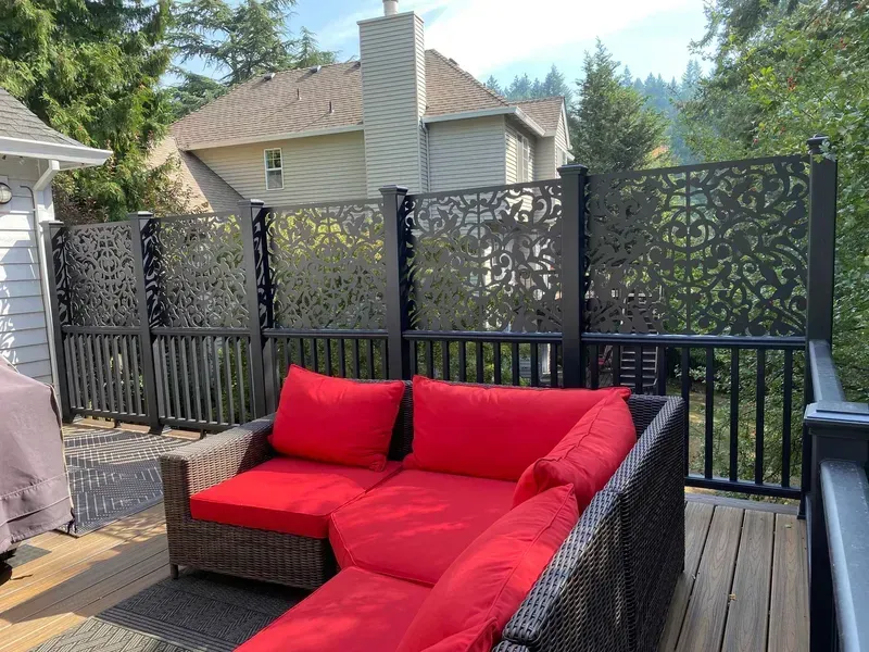 Outdoor deck with a sectional sofa, decorative black privacy screens, and a house in the background.