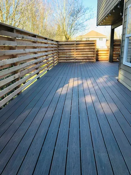 Wooden deck with horizontal wood fence, attached to a house with a window, outdoors.
