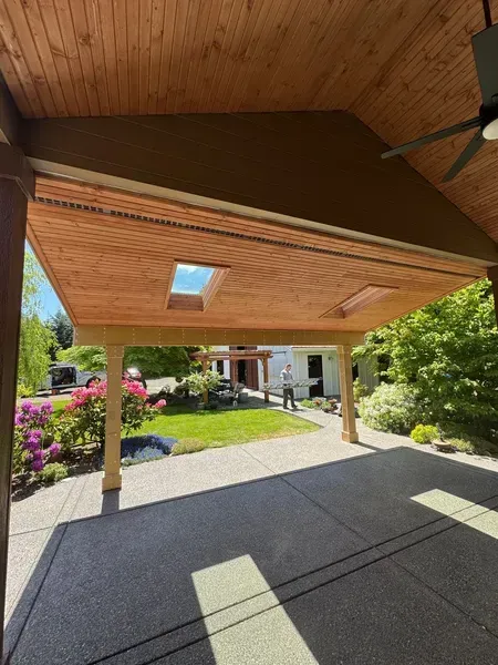 Covered patio with wood ceiling, skylights, and concrete floor, overlooking a yard and house.