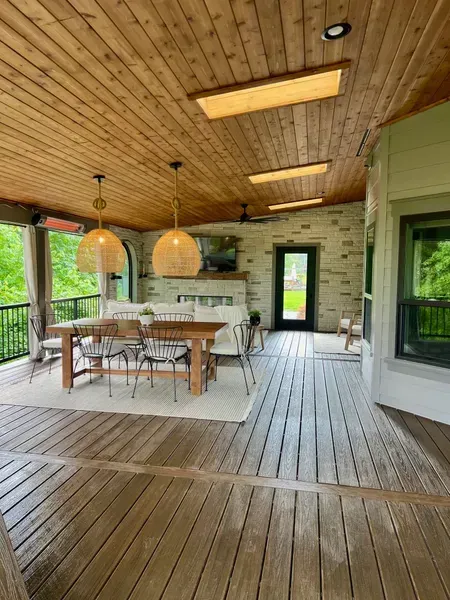 Covered wooden deck with dining table, hanging lights, and stone accent wall.