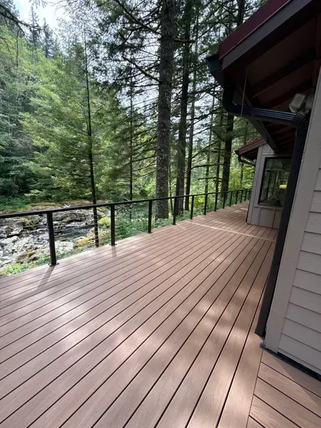 Wooden deck with black railings next to a forest and a house.