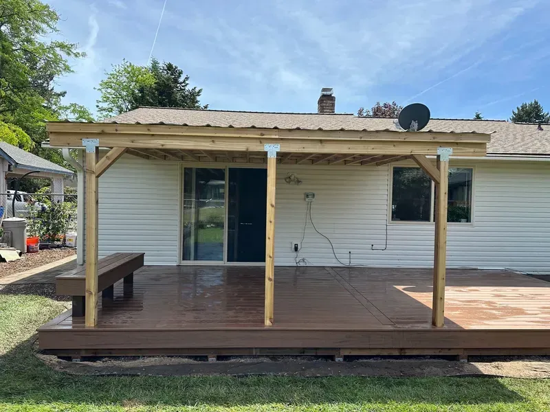 Wooden deck with attached canopy. Brown deck, light-colored wooden frame, metal roof. Sliding glass door visible.