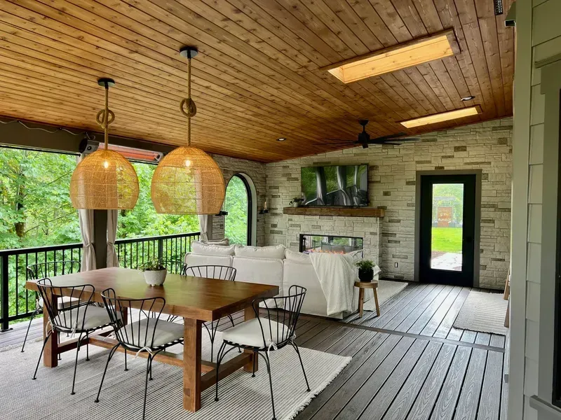 Covered patio with dining table, seating area, fireplace, and natural stone wall; wood ceiling.
