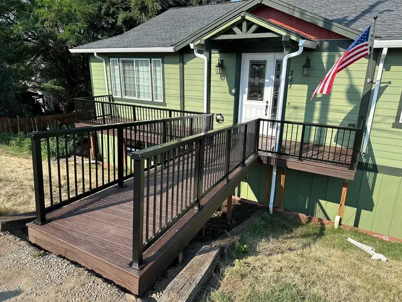 Green house with brown deck and black railing; American flag.