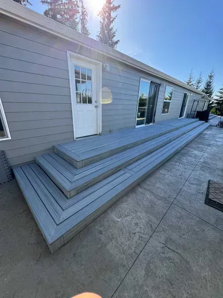 Gray composite deck with three steps leading to a white door; attached to a light gray house.