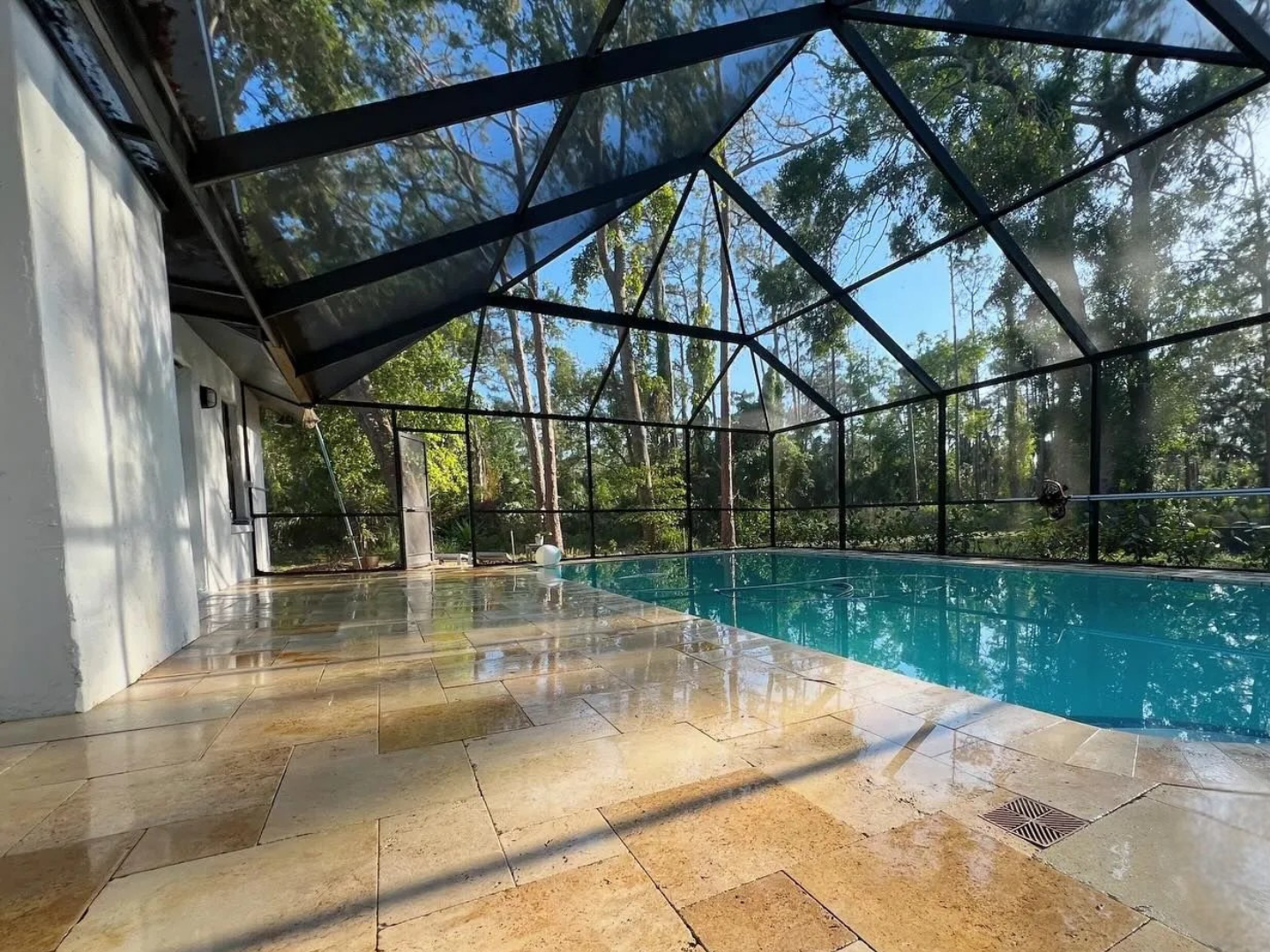 Screened-in backyard pool with tan patio and blue water under a glass roof