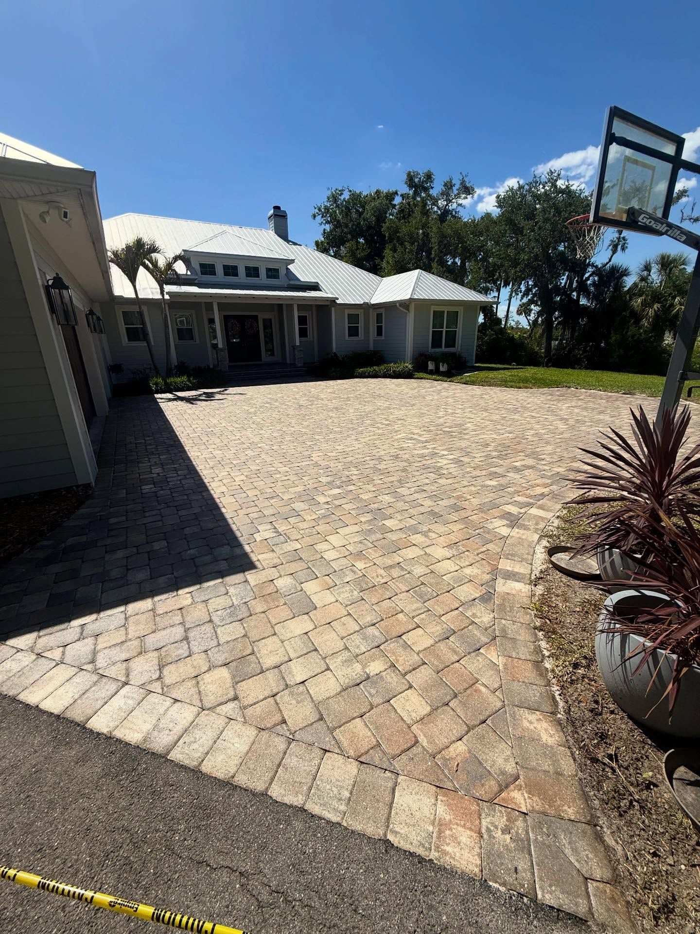Large paved driveway leading to a white house with a front porch under a clear blue sky