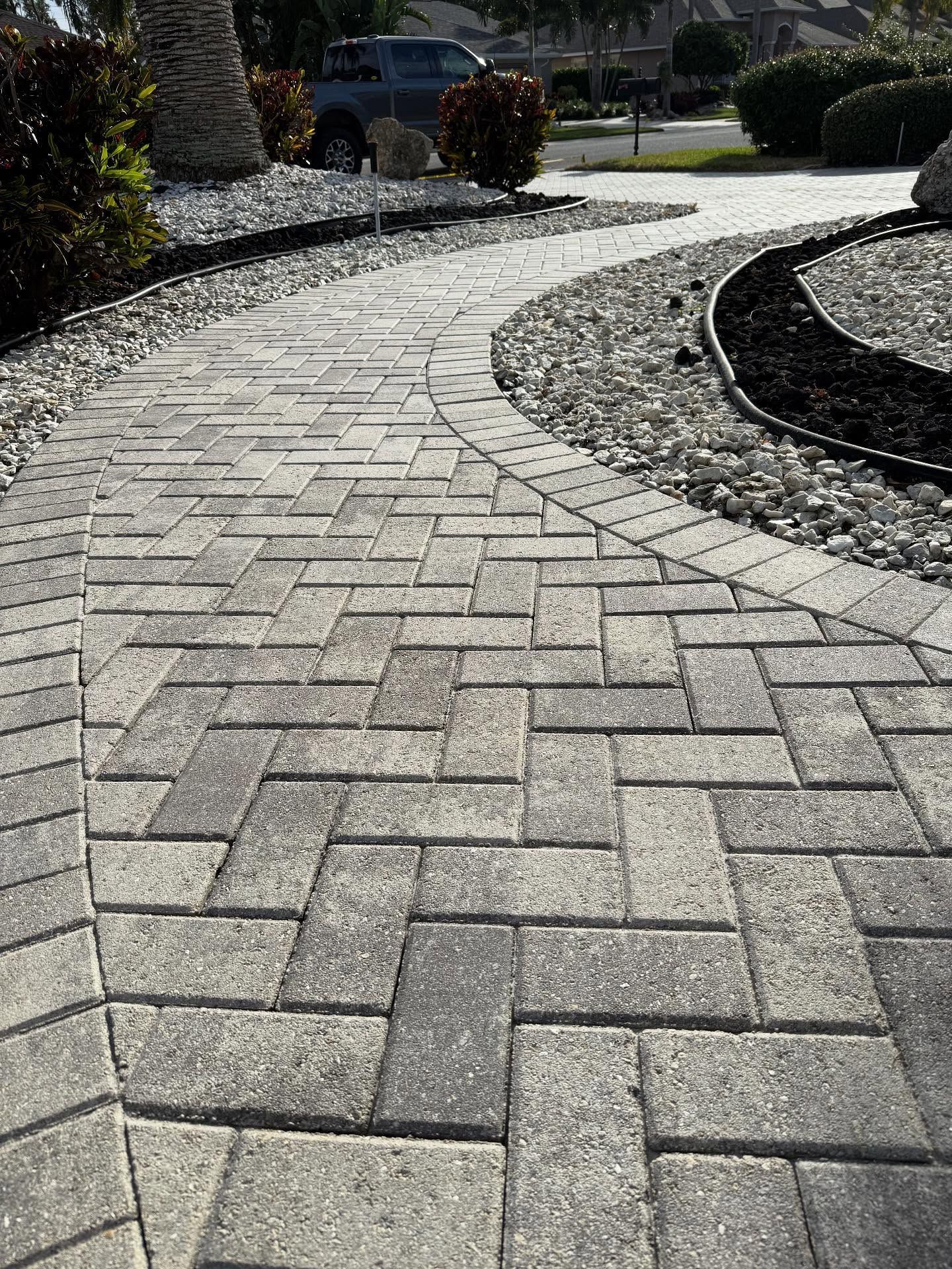 Curved stone paver walkway beside landscaped rocks and shrubs in bright sunlight