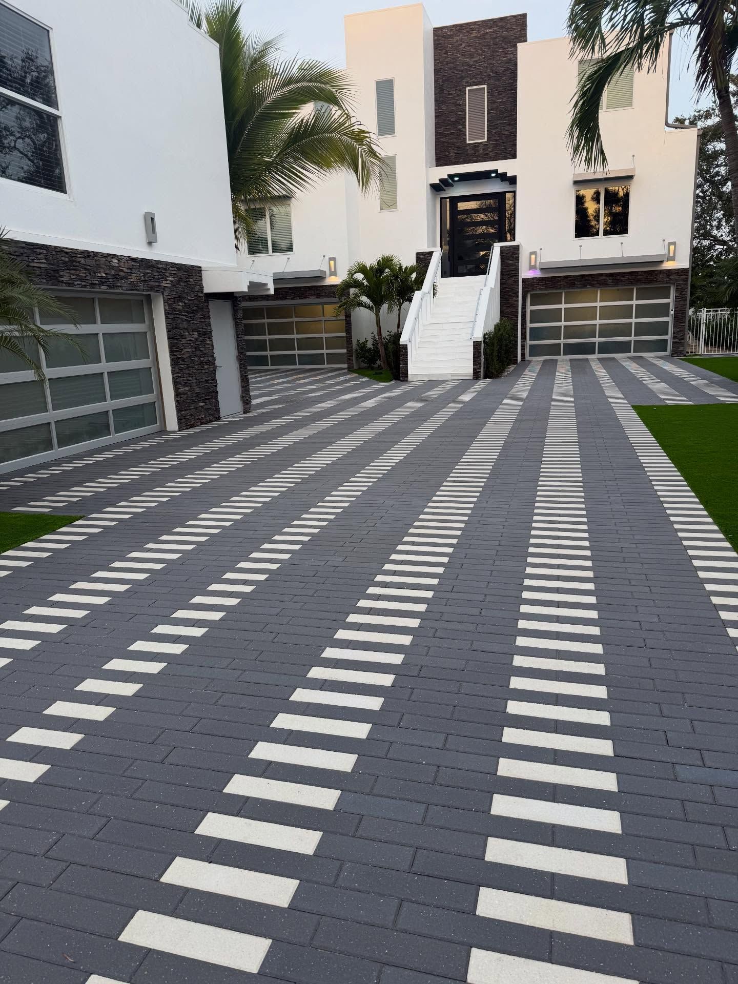 Modern house driveway with patterned gray pavers and white stripe inlays leading to the entrance