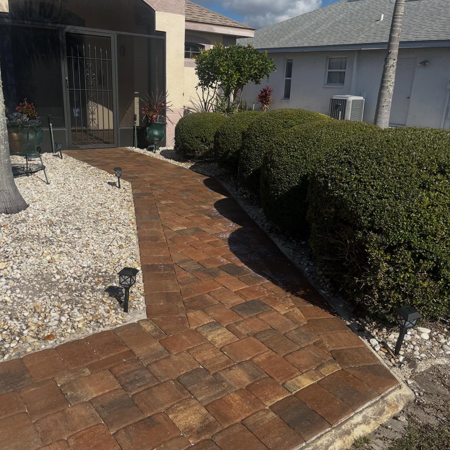 Brick walkway curving past white gravel and trimmed hedges beside a house entrance