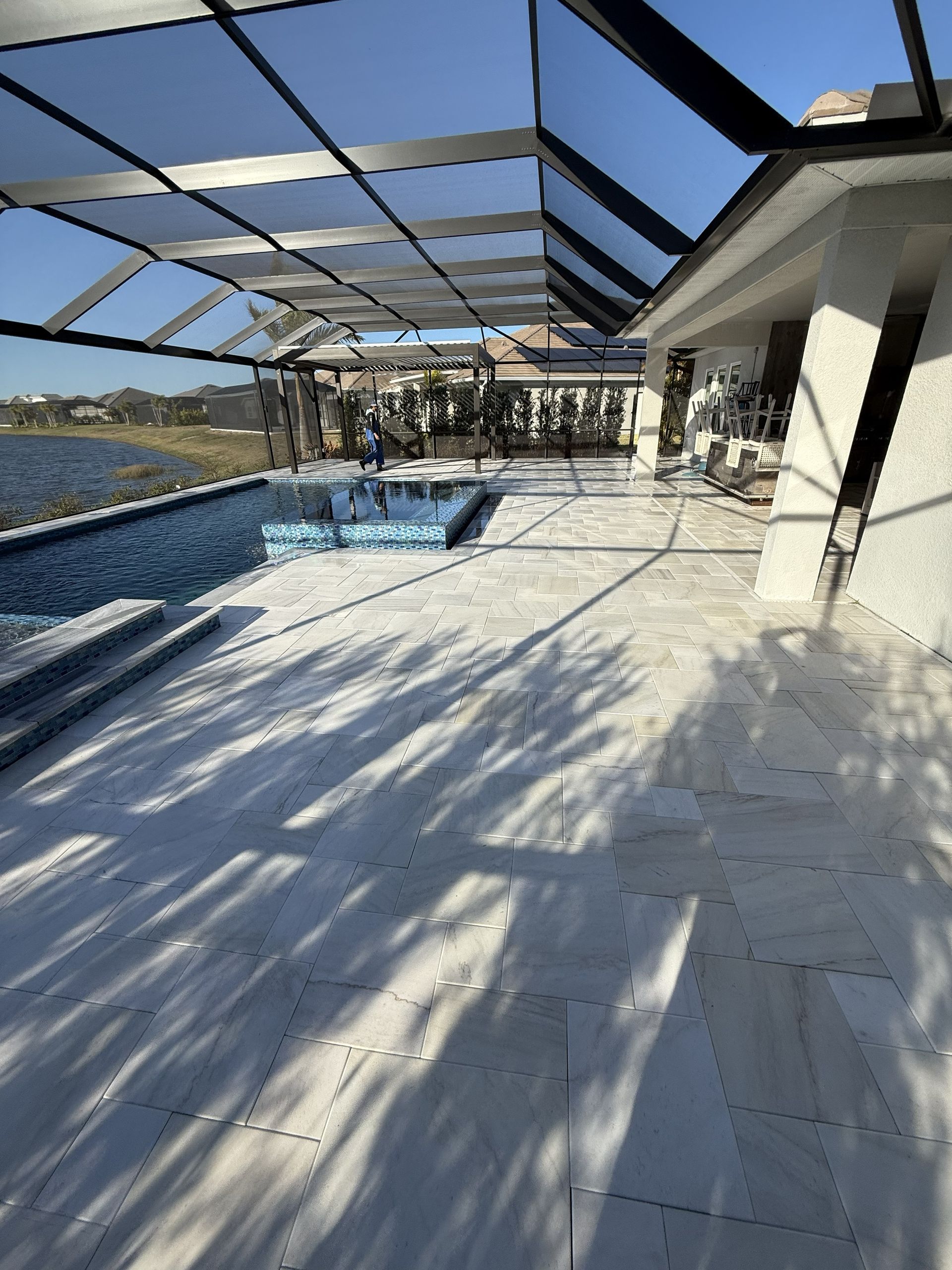 Sunny poolside patio with screened enclosure, lounge chairs, and blue pool by the water