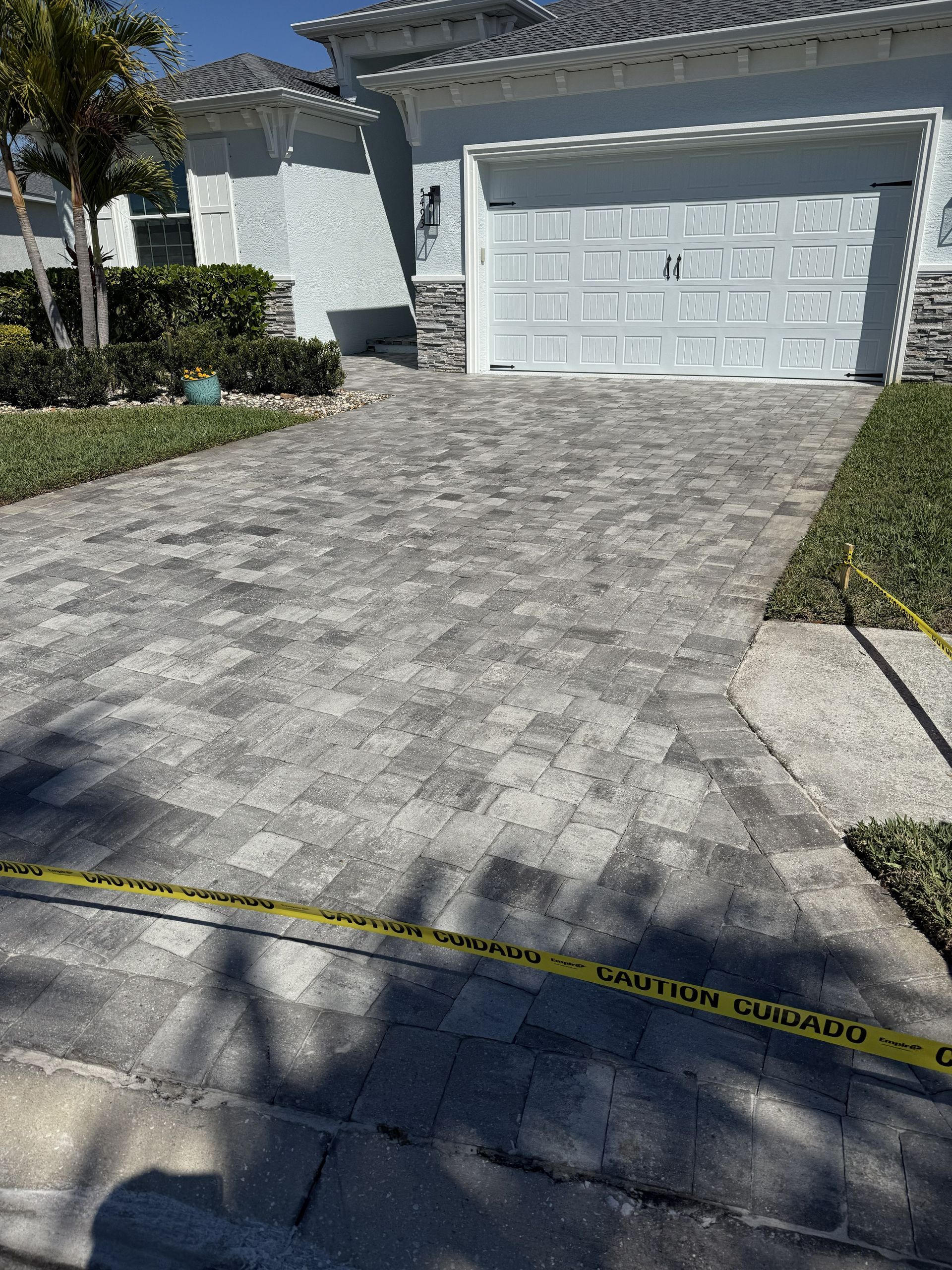 Driveway paved with gray stone leading to a white garage, with caution tape across the foreground.