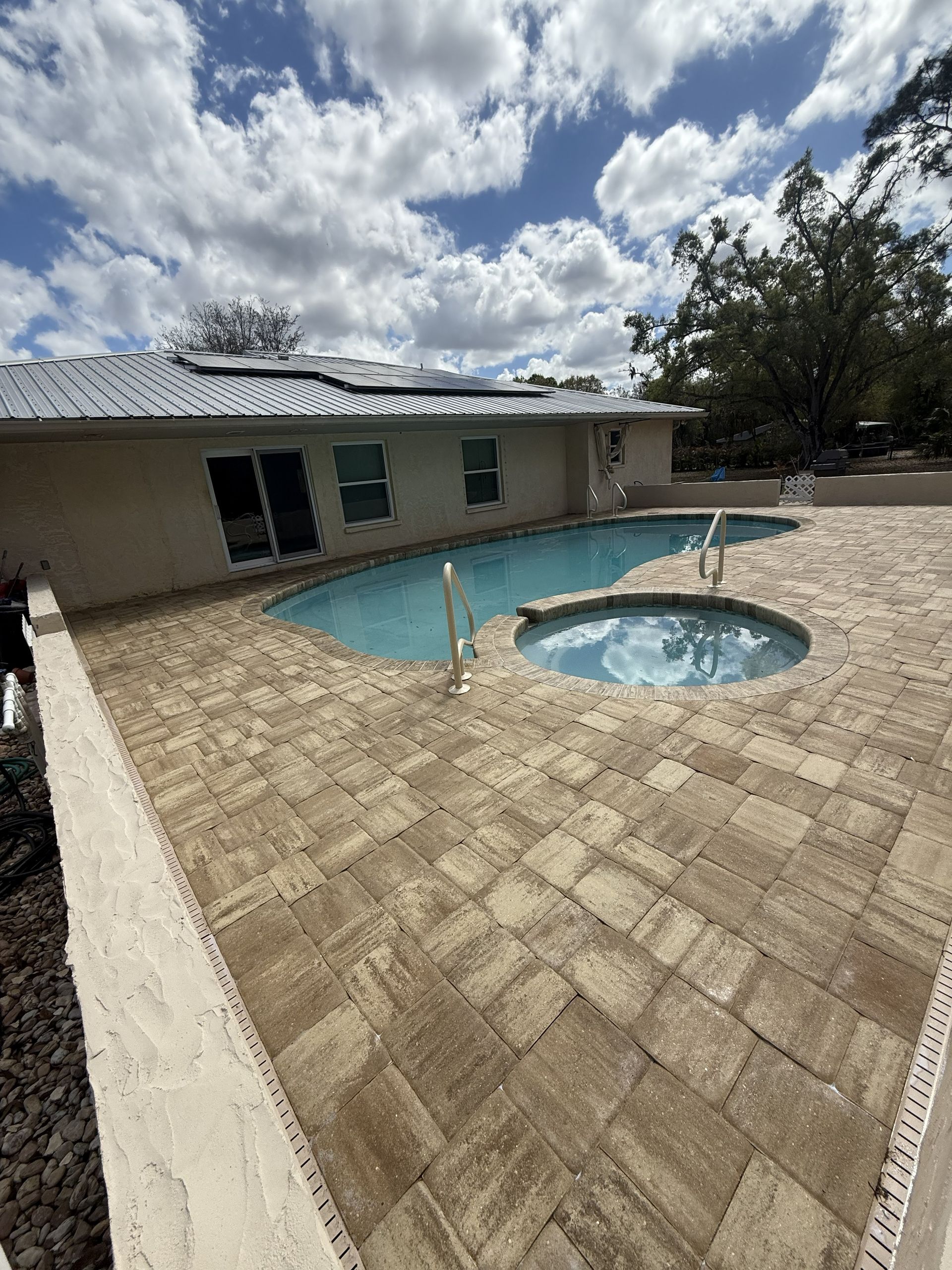 Patio with paver stones, a house, and a small swimming pool under a partly cloudy sky