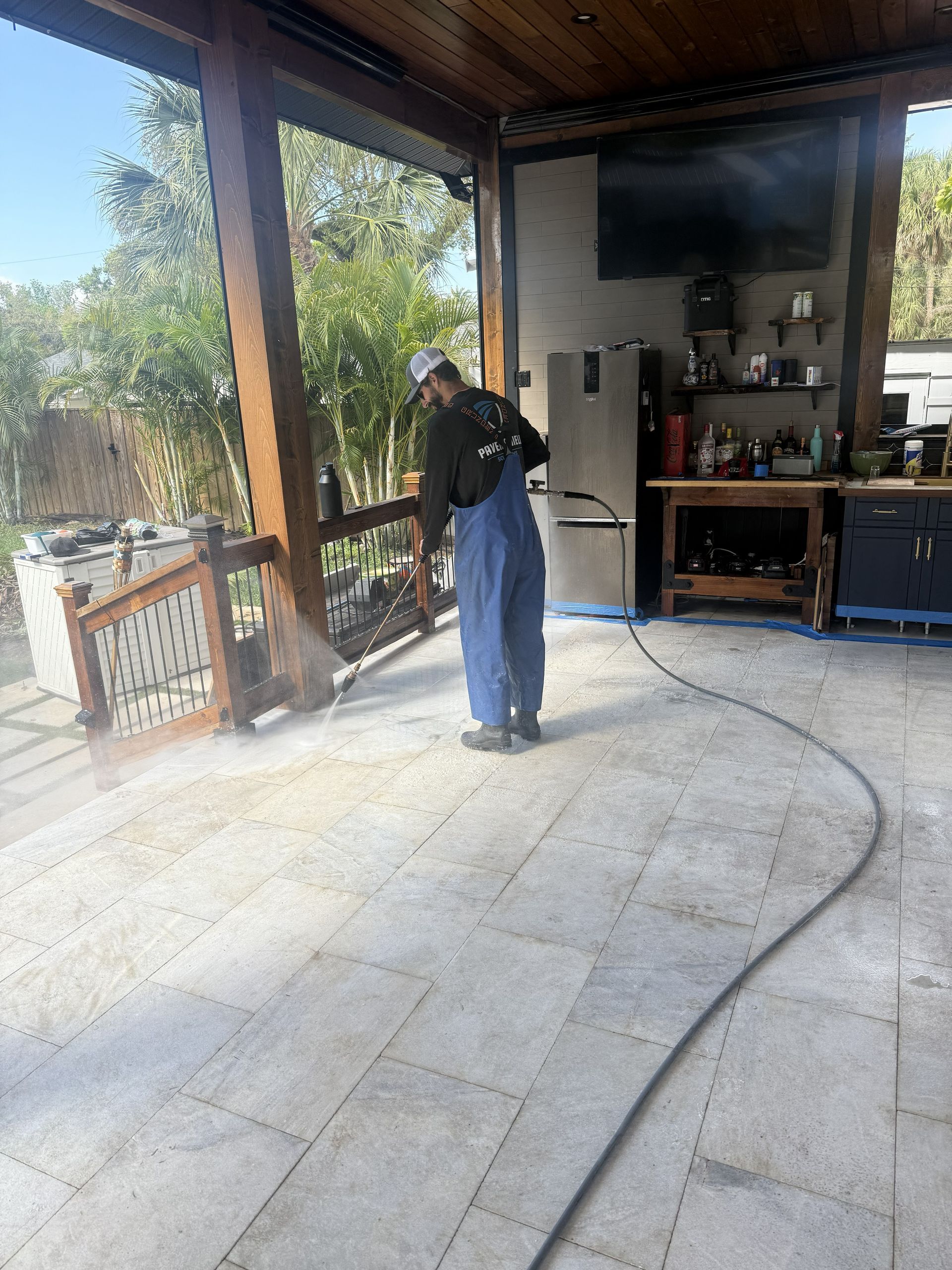 Person using a pressure washer on a concrete patio under a covered porch