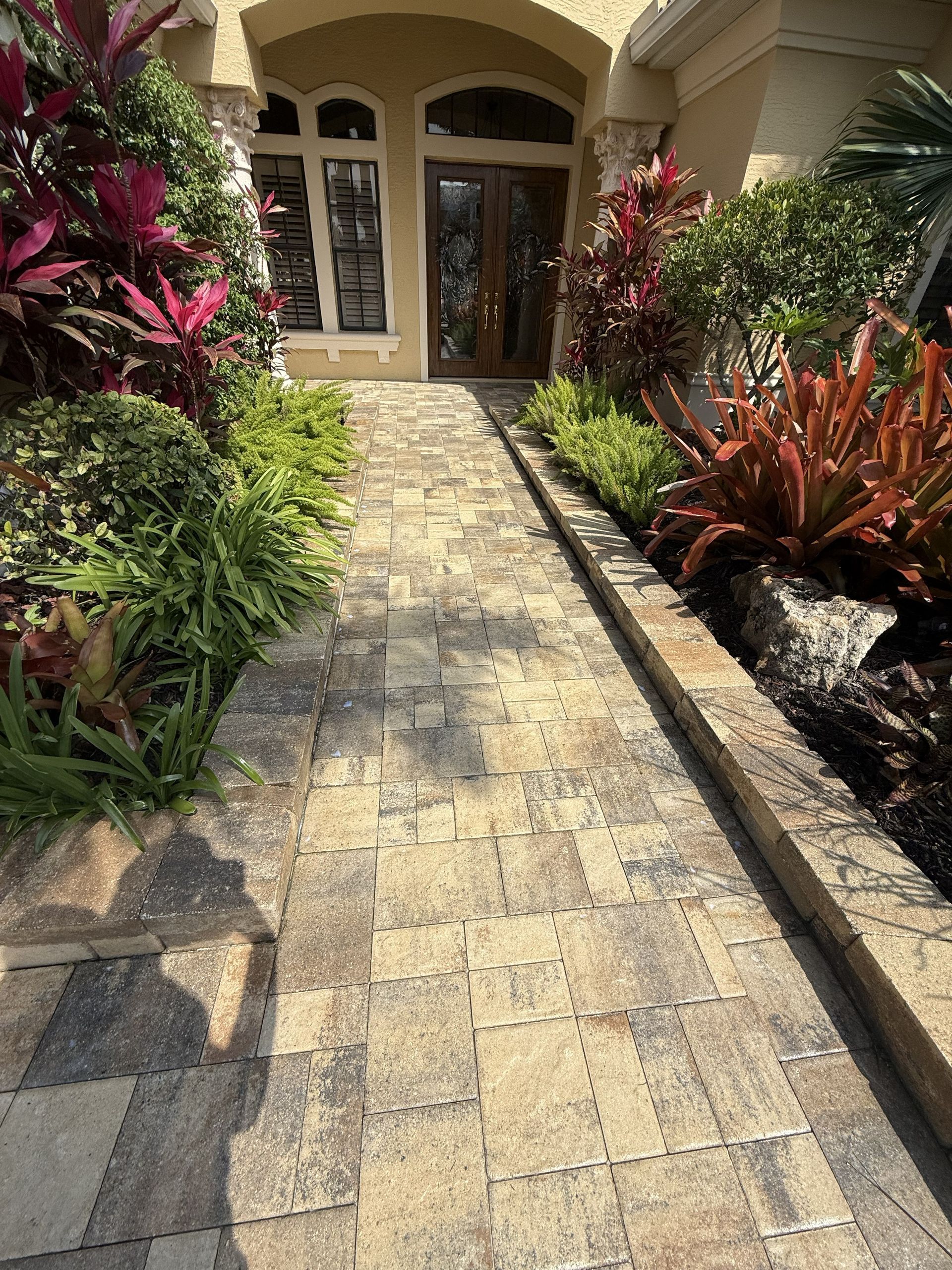 Stone walkway leading to a front door, bordered by lush red and green tropical landscaping