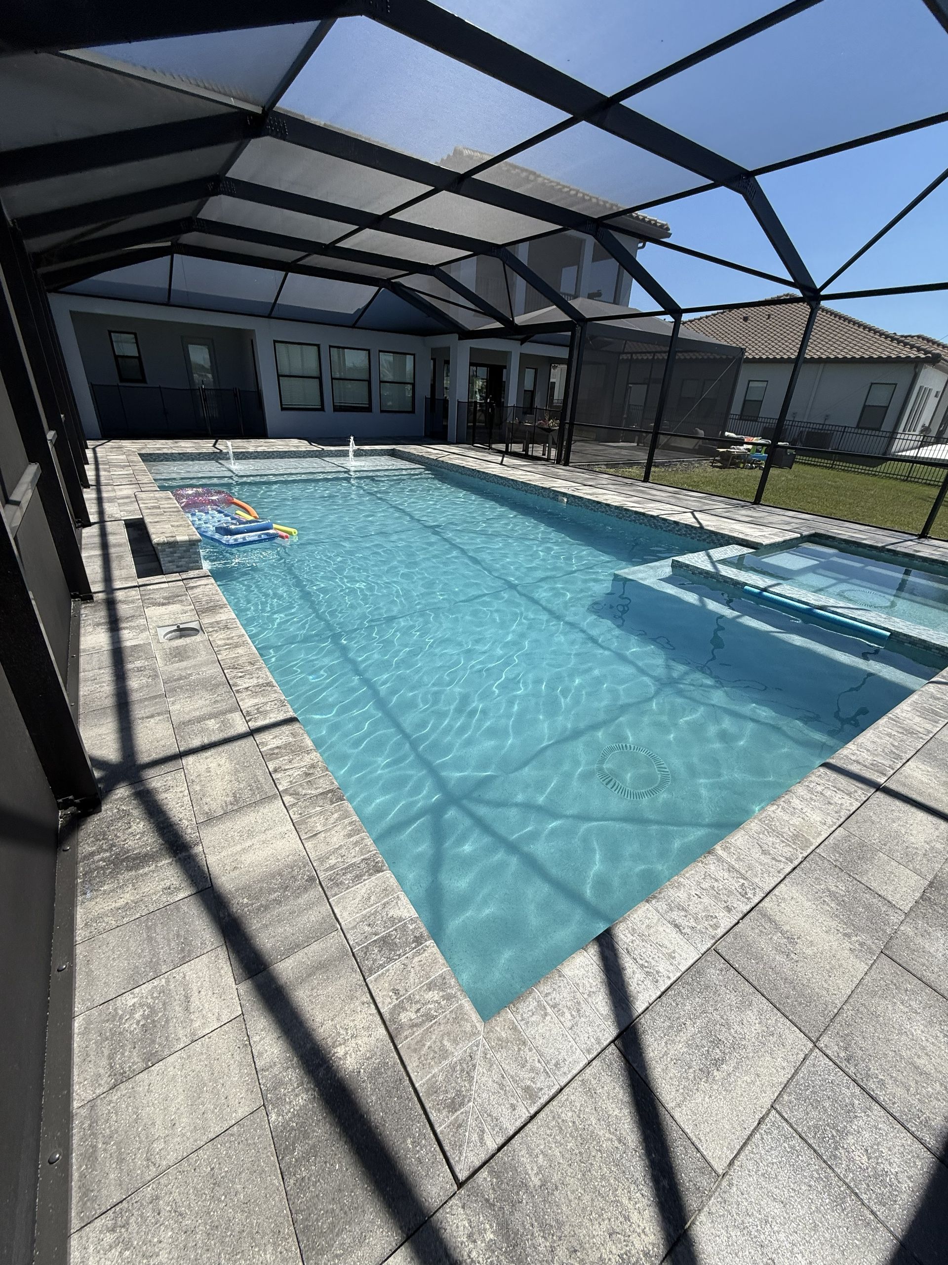 Covered backyard pool with blue water, lounge chairs, and a screened patio under a bright blue sky