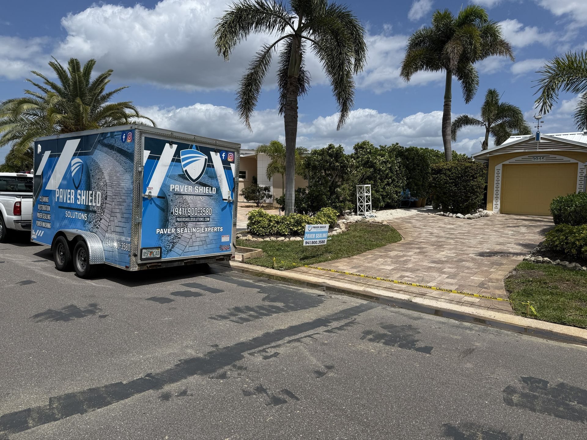 Blue service van parked on a residential street beside a stone driveway and palm trees