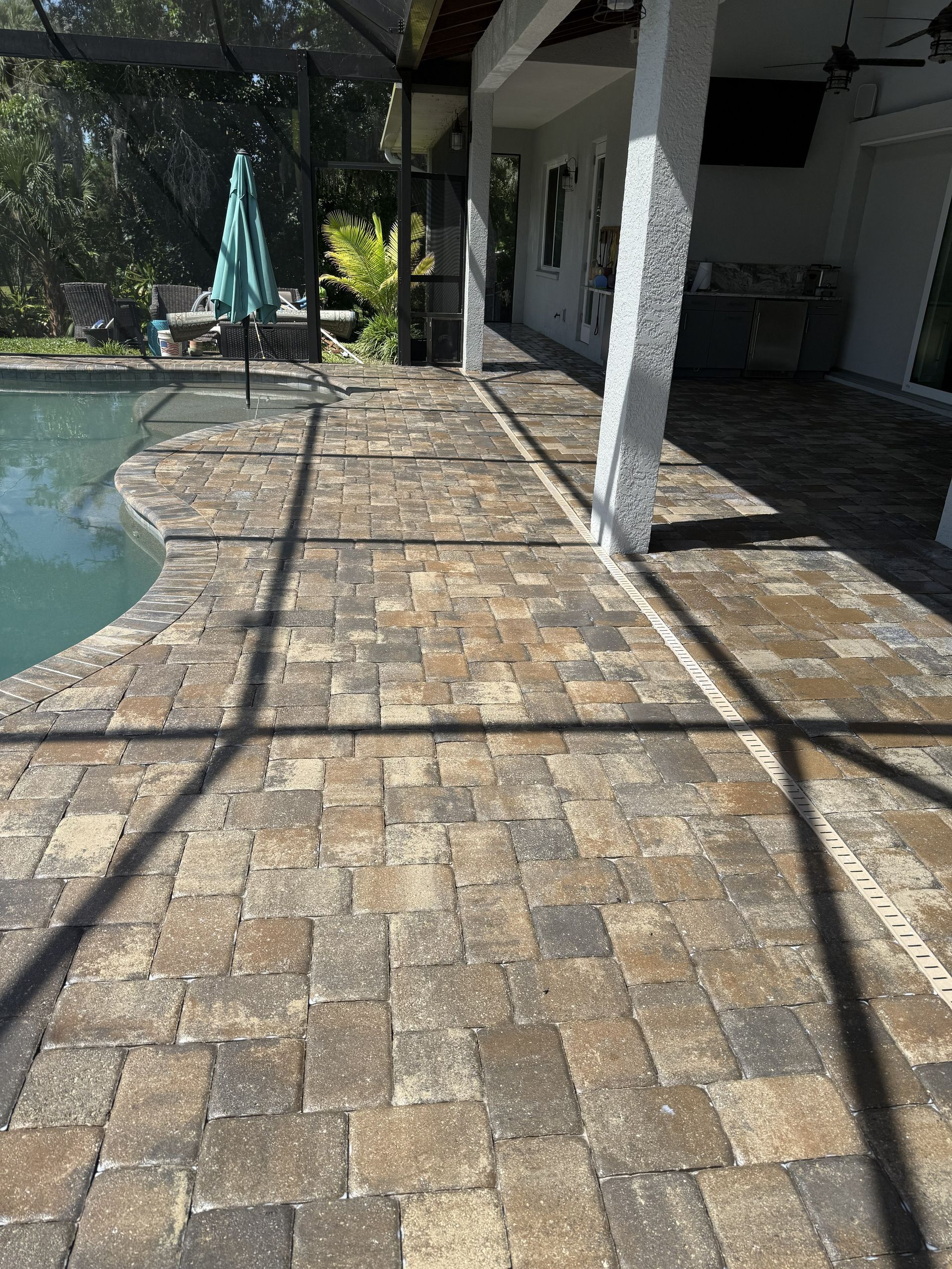 Brick patio beside a pool, with white columns and a shaded outdoor seating area.