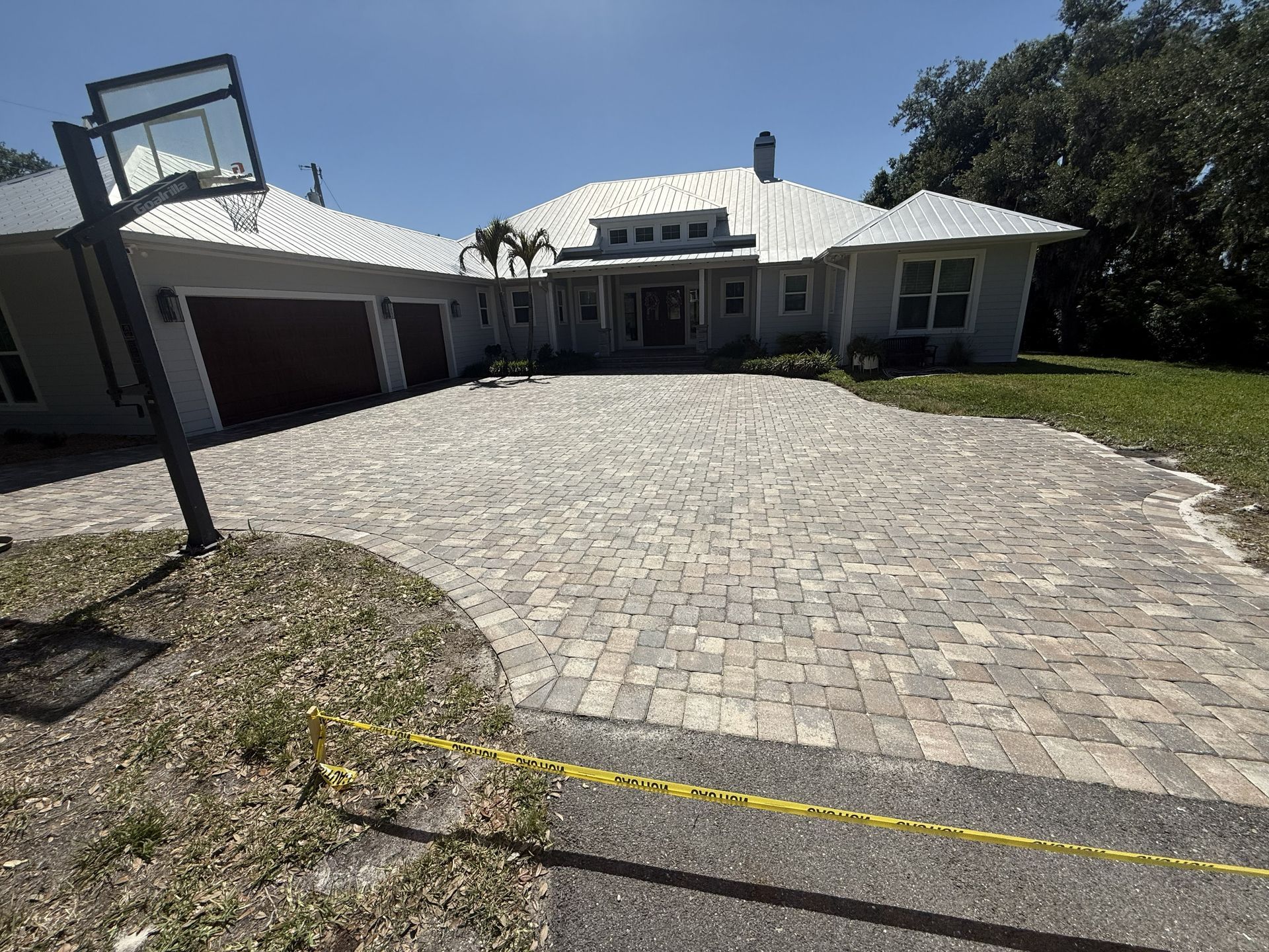 Large paved driveway leading to a white house with a garage under a bright blue sky.