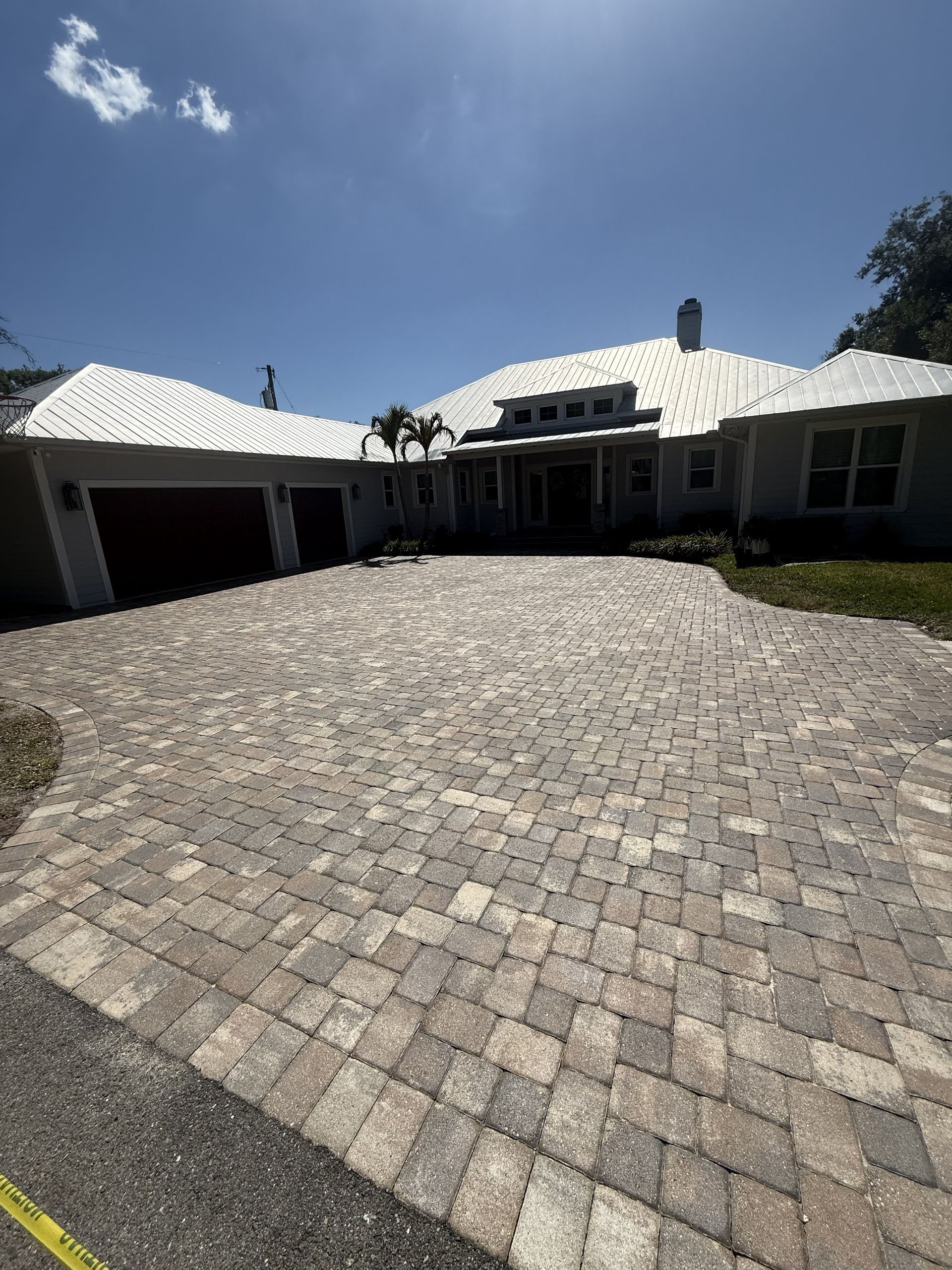 Stone-paver driveway leading to a suburban house with white roof and garage under a blue sky
