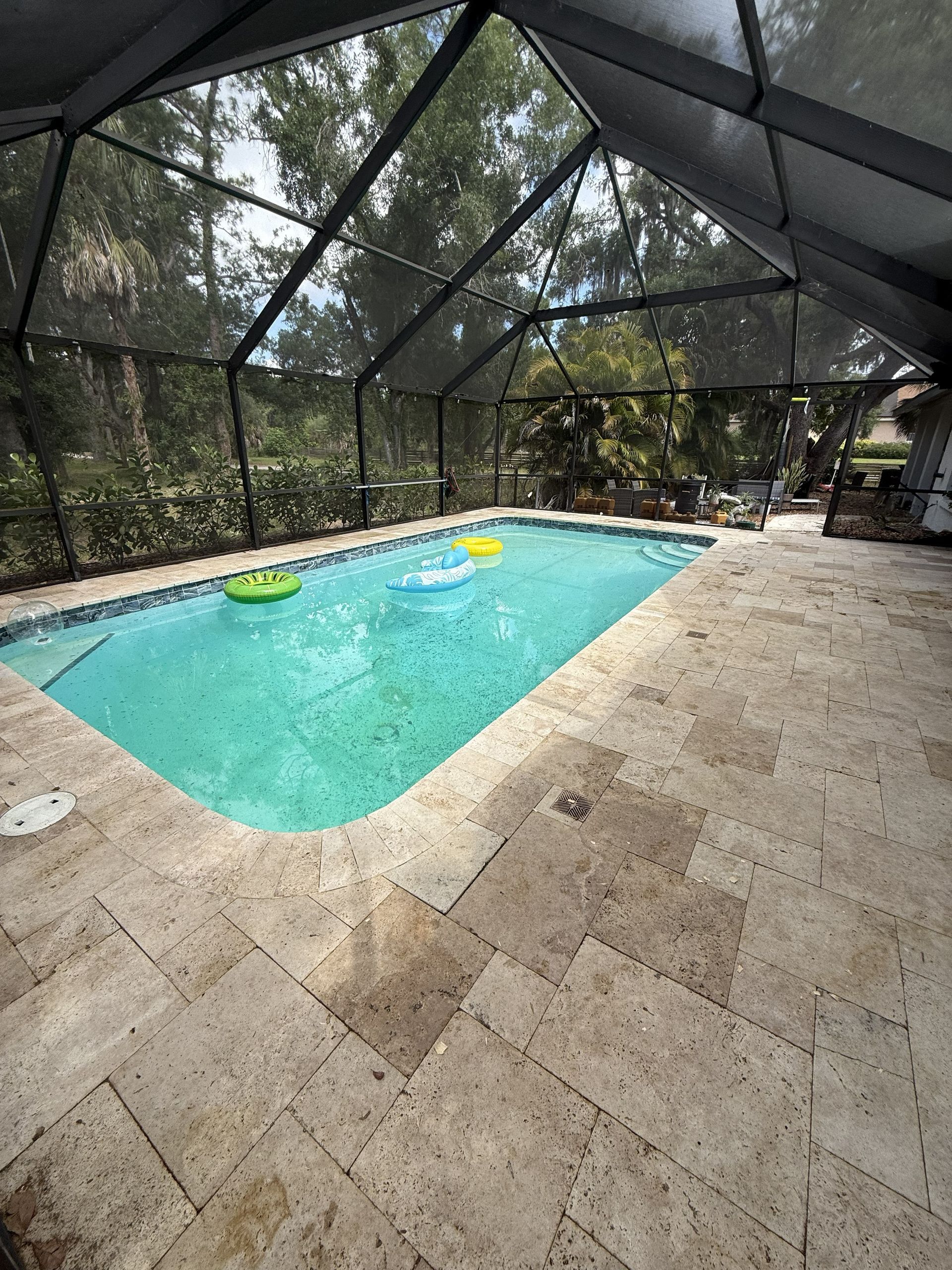 Screened-in backyard pool with turquoise water and stone patio, with floating pool rings.