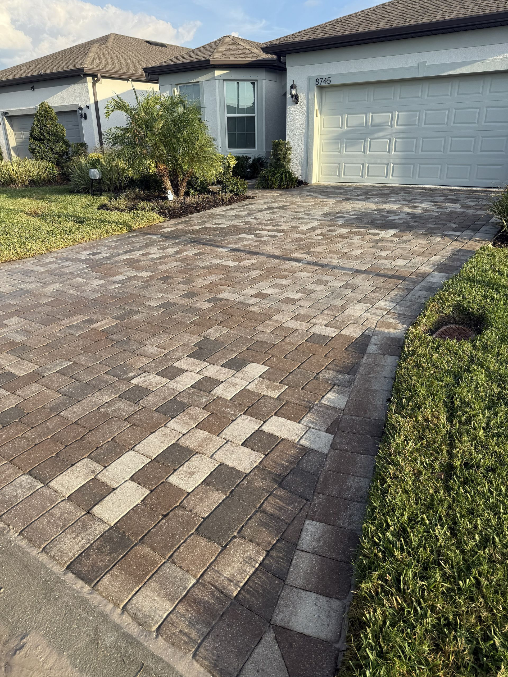 Brick-paved driveway leading to a suburban house with a double garage and front garden