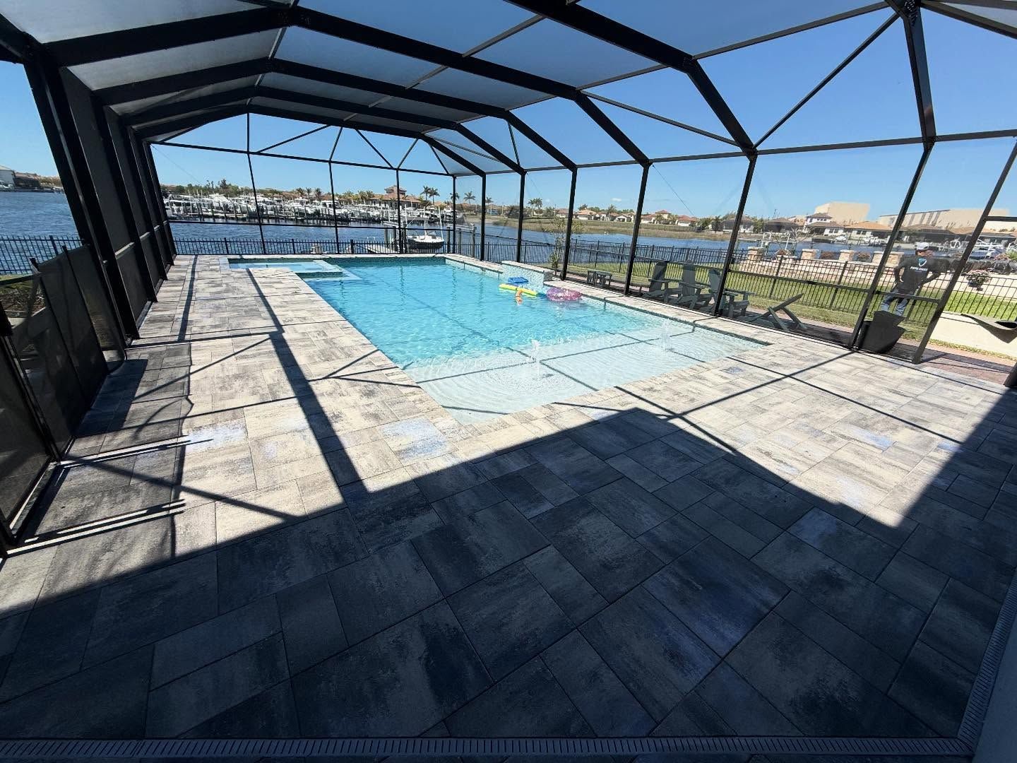 Screened-in backyard pool with stone deck and lounge area overlooking water and homes