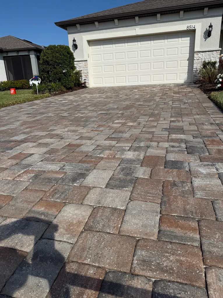 Brick paver driveway leading to a white garage door in a sunny suburban home.