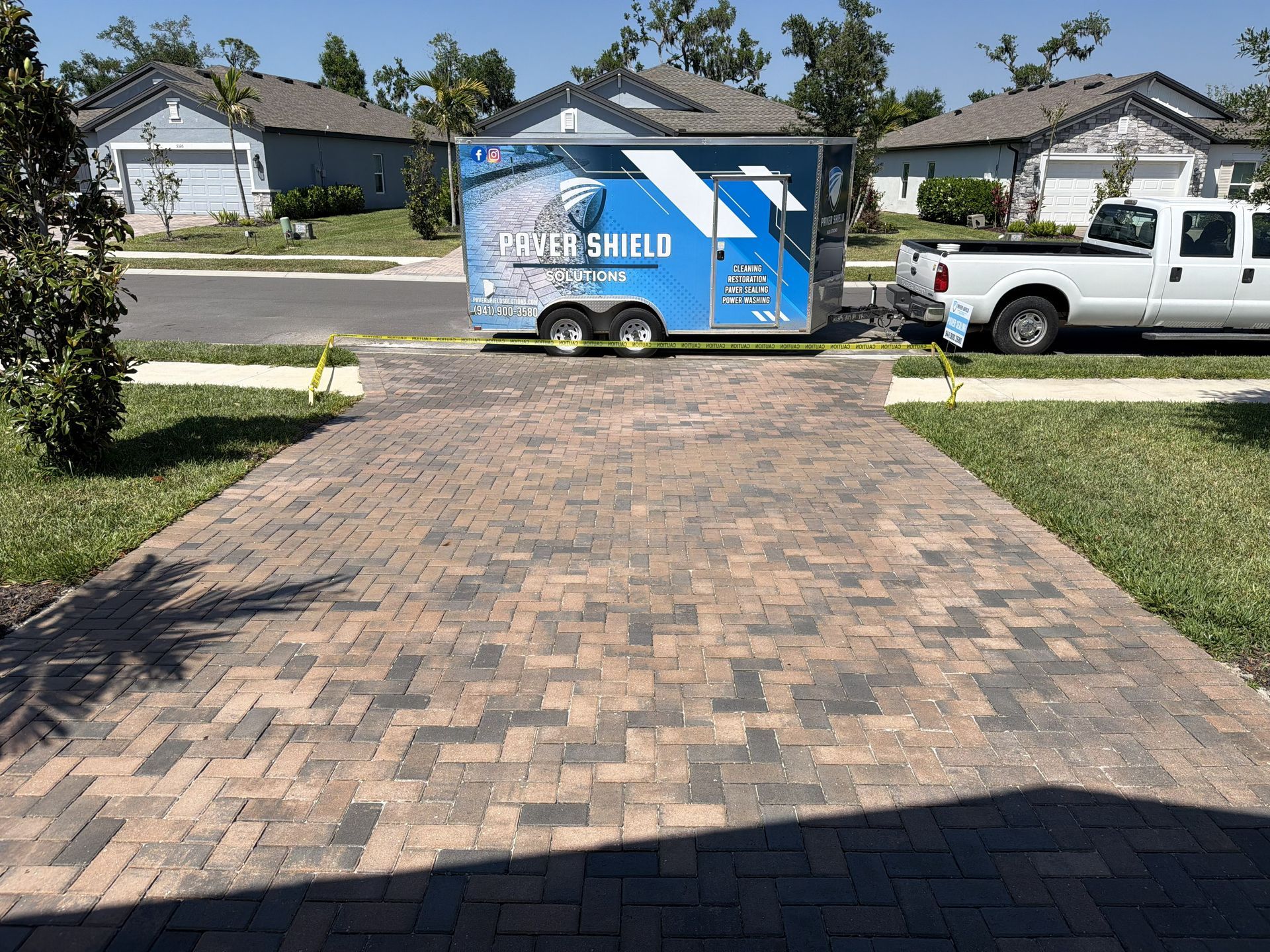 Driveway with a blue Fiber Shield trailer and a white pickup truck in a suburban neighborhood.