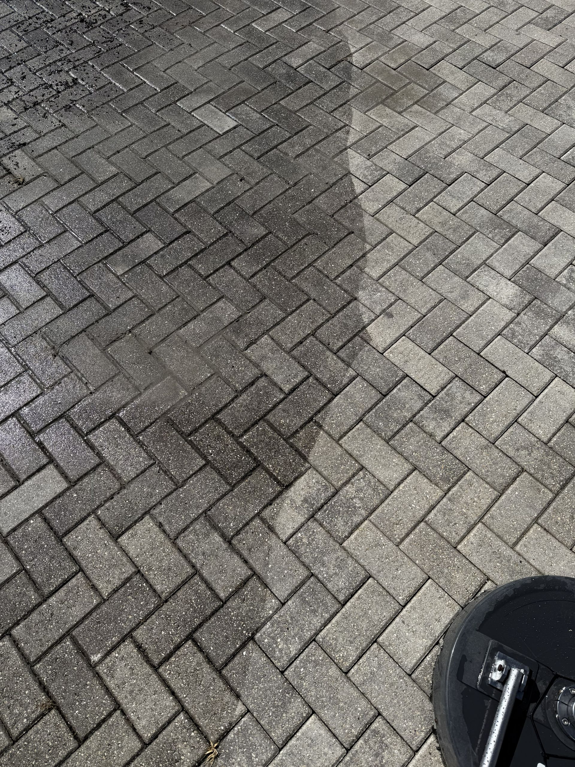 Wet herringbone brick pavement with a dark damp patch and part of a wheel at bottom right