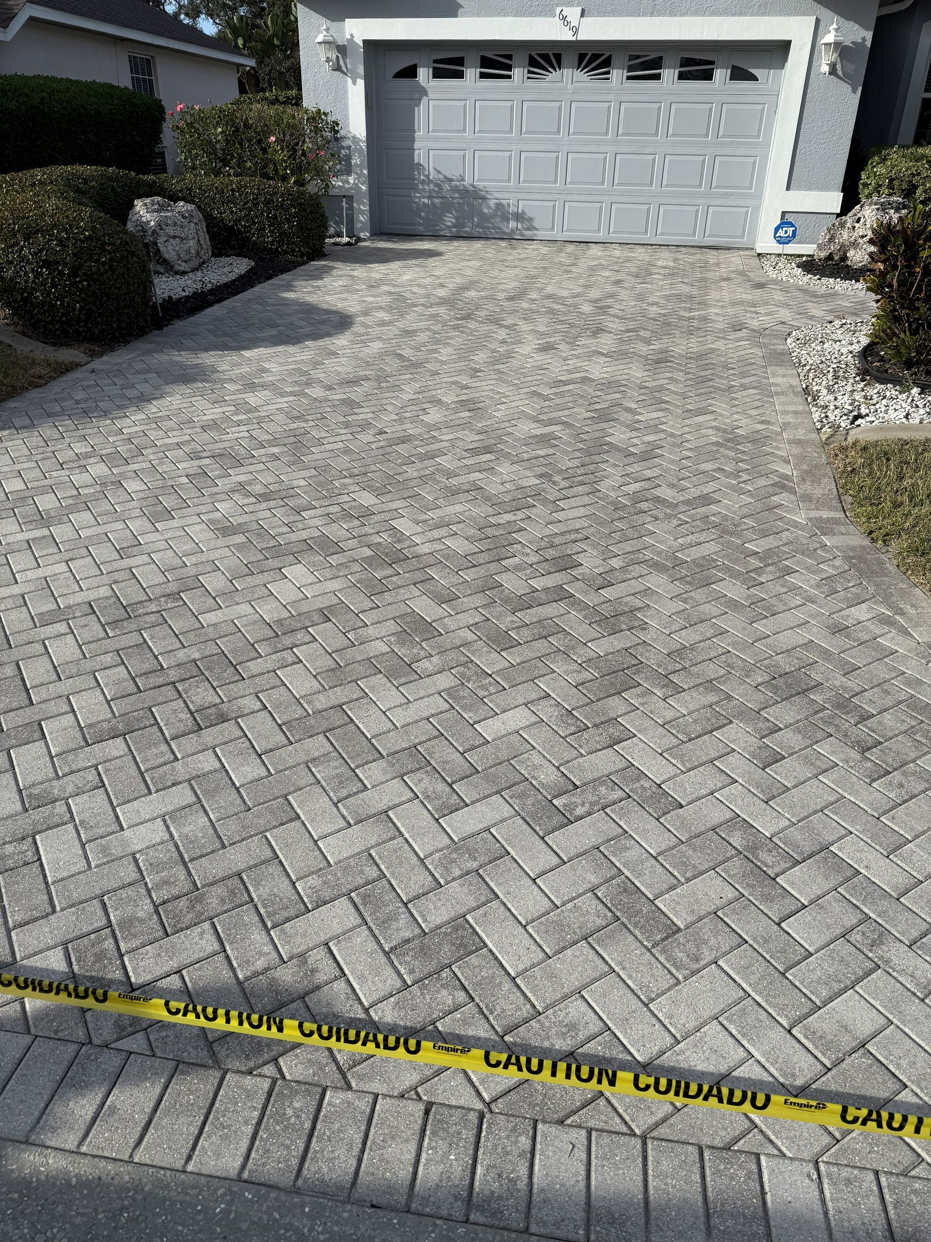 Brick-paver driveway leading to a white garage, marked with yellow caution tape in front.