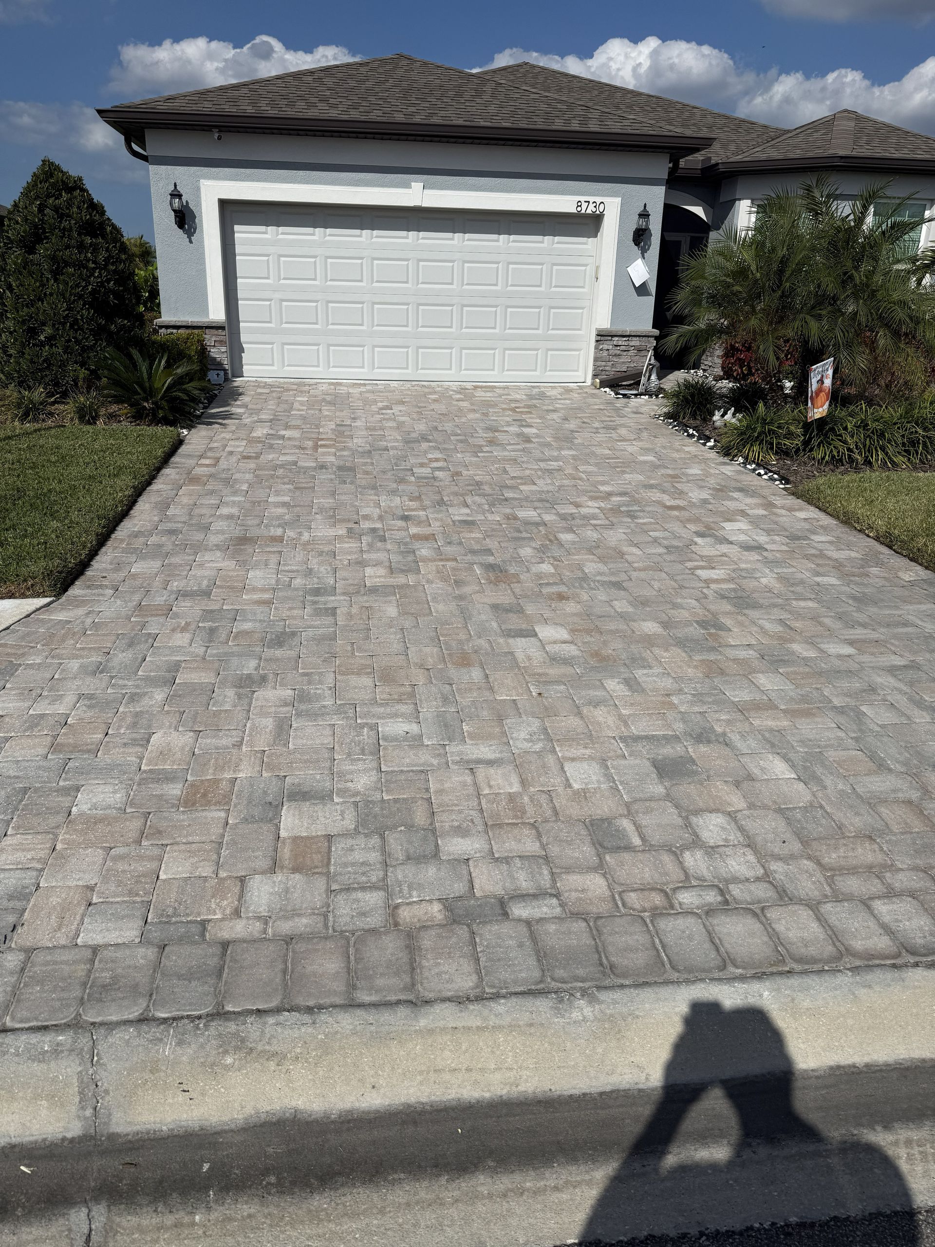 Stone-paver driveway leading to a white garage door on a sunny suburban house