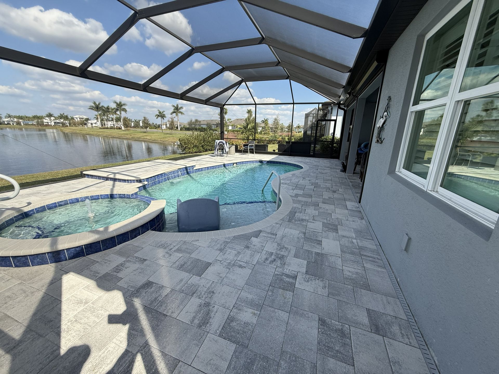 Screened backyard patio with a pool, spa, and gray pavers beside a house and lake view