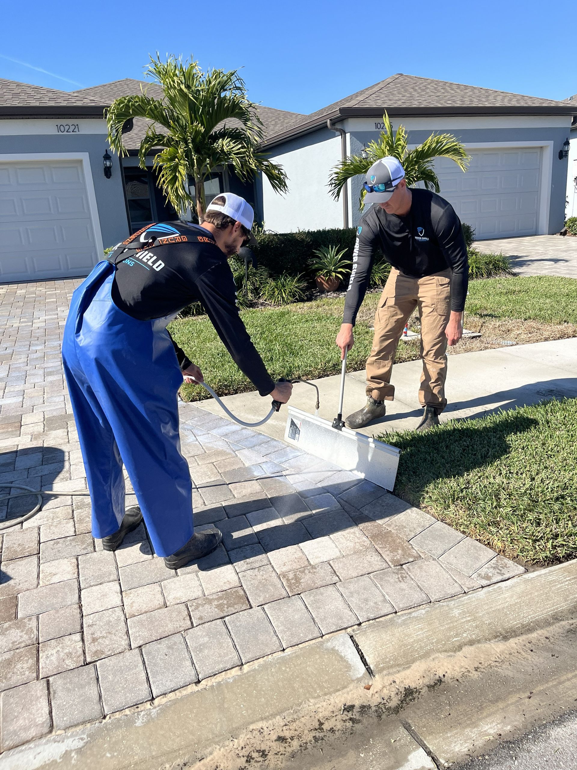 Two workers in a suburban driveway spreading concrete by a curb beside a garage.