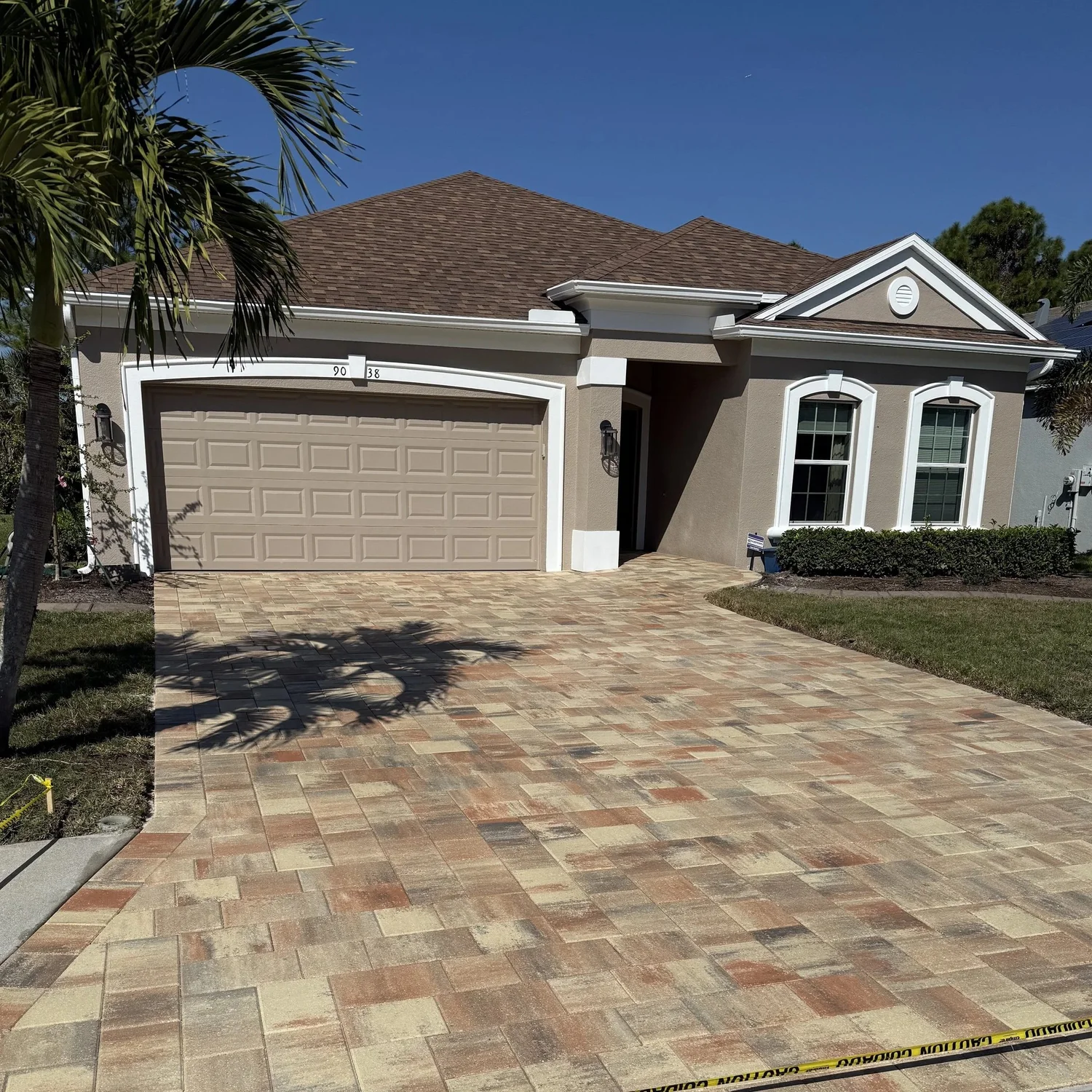 Single-story stucco house with a two-car garage and tiled driveway under a clear blue sky