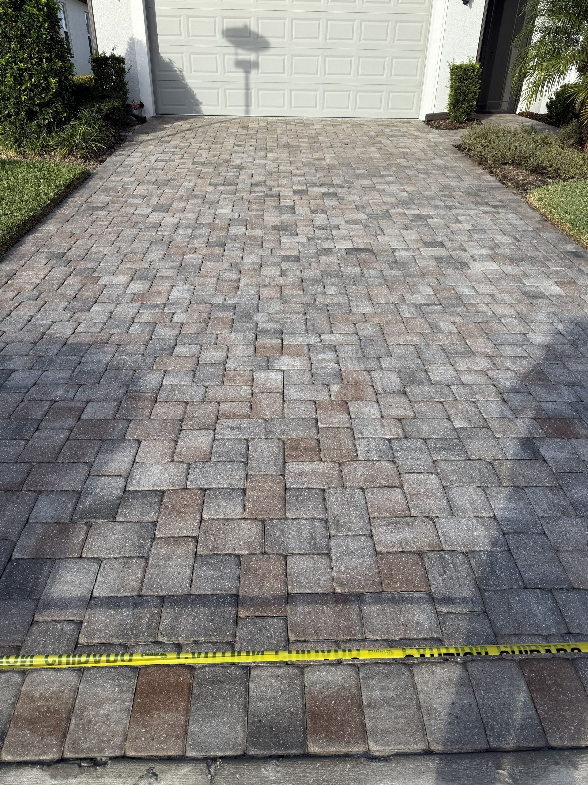 Brick paver driveway leading to a white garage door, with a yellow tape measure across the bottom edge.