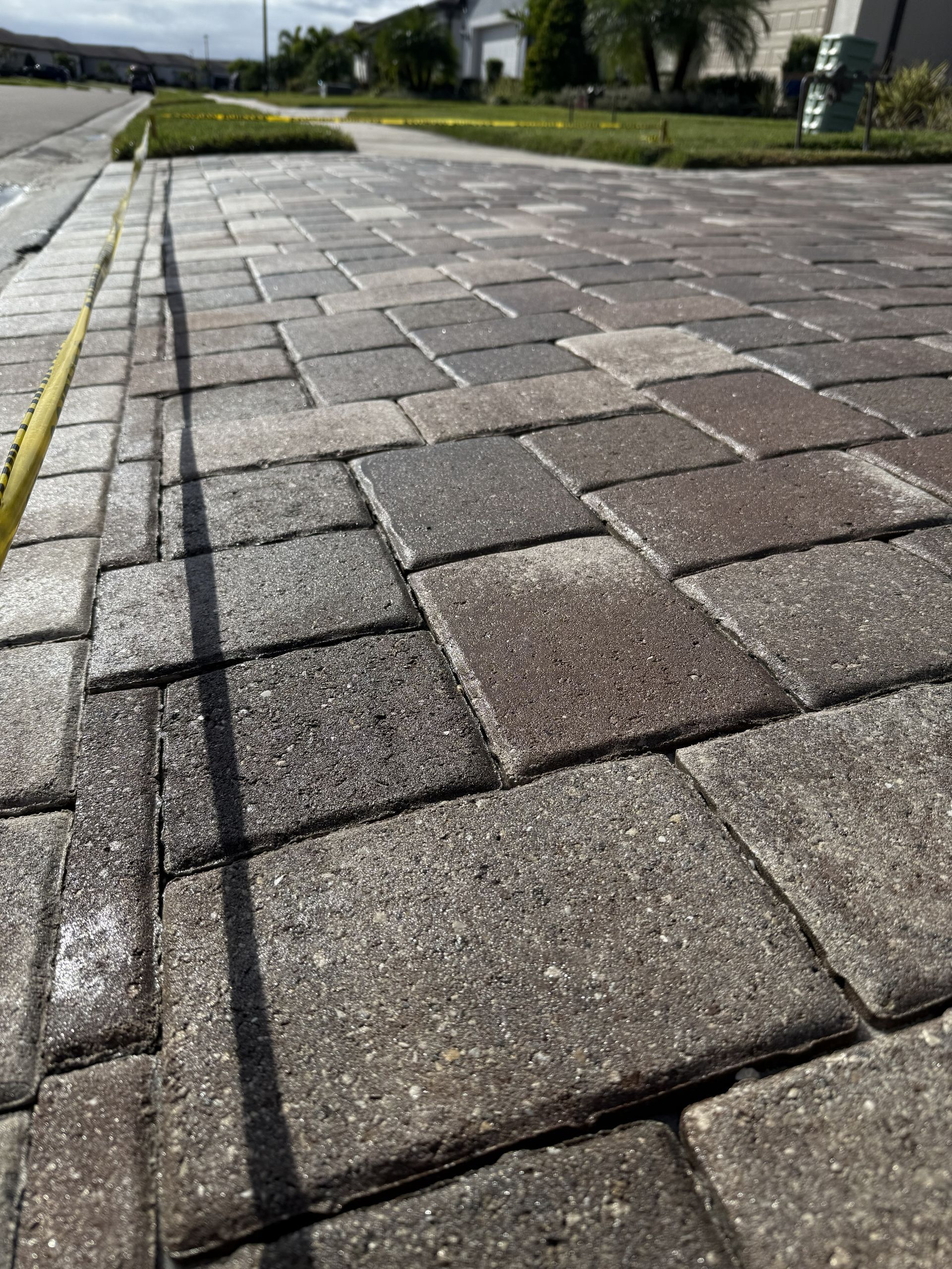 Damaged brick sidewalk with uneven pavers along a street curb under cloudy sky