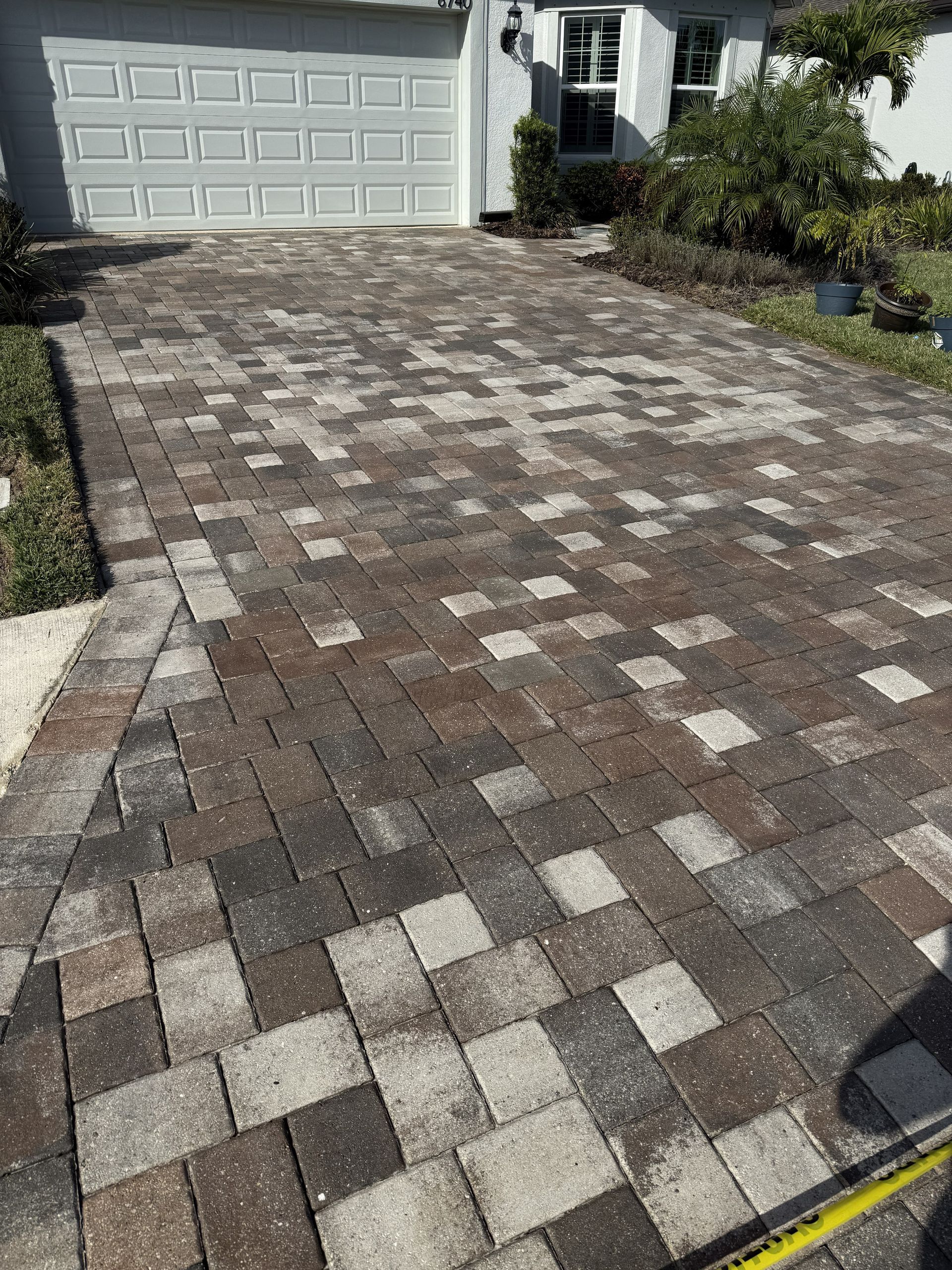 Paver driveway leading to a white garage with a patchwork of gray, tan, and brown stones.