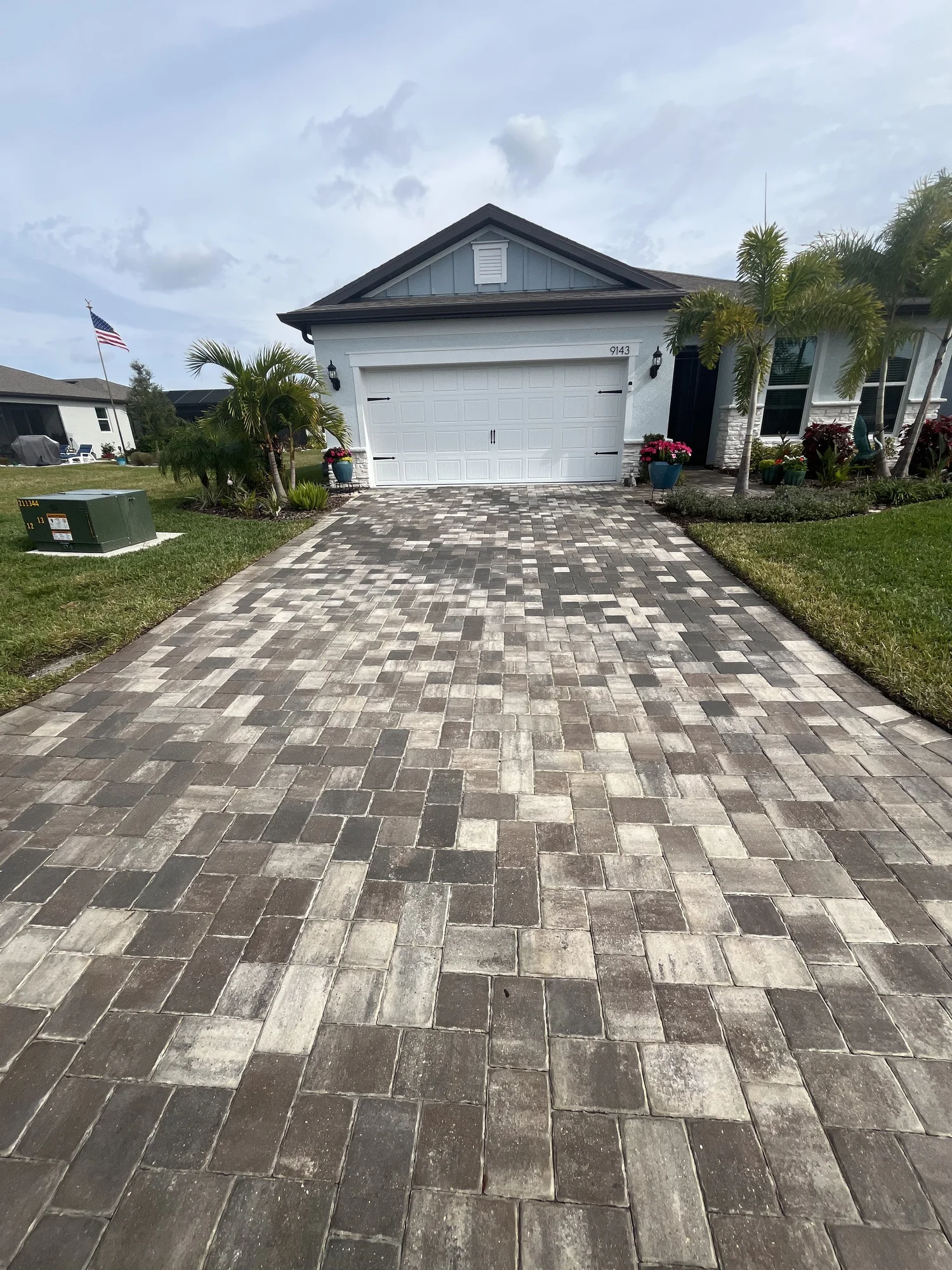 Driveway leading to a white house with a two-car garage and a paver path in the foreground.