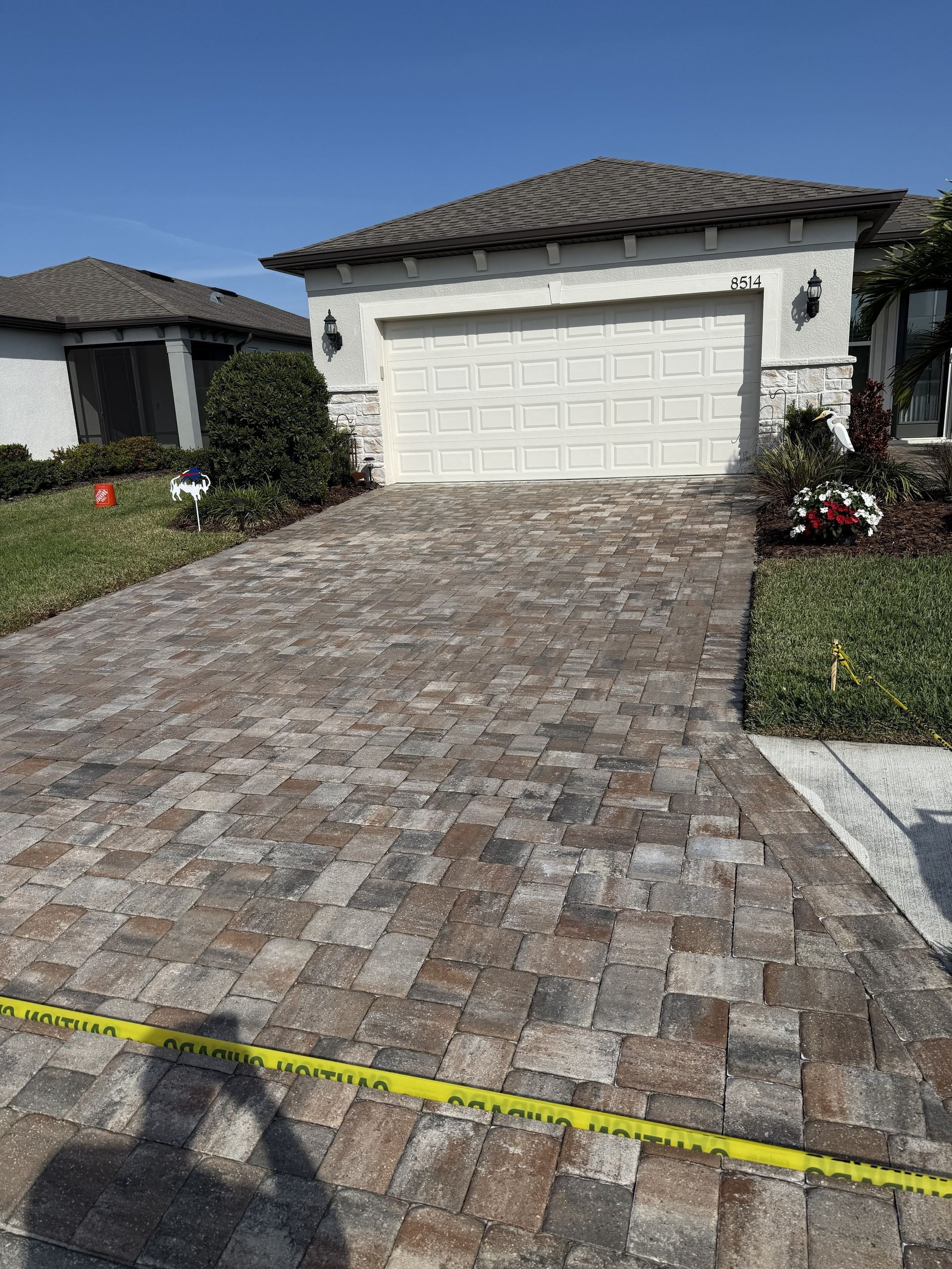 Brick-paved driveway leading to a white garage in a suburban house with a tiled roof.