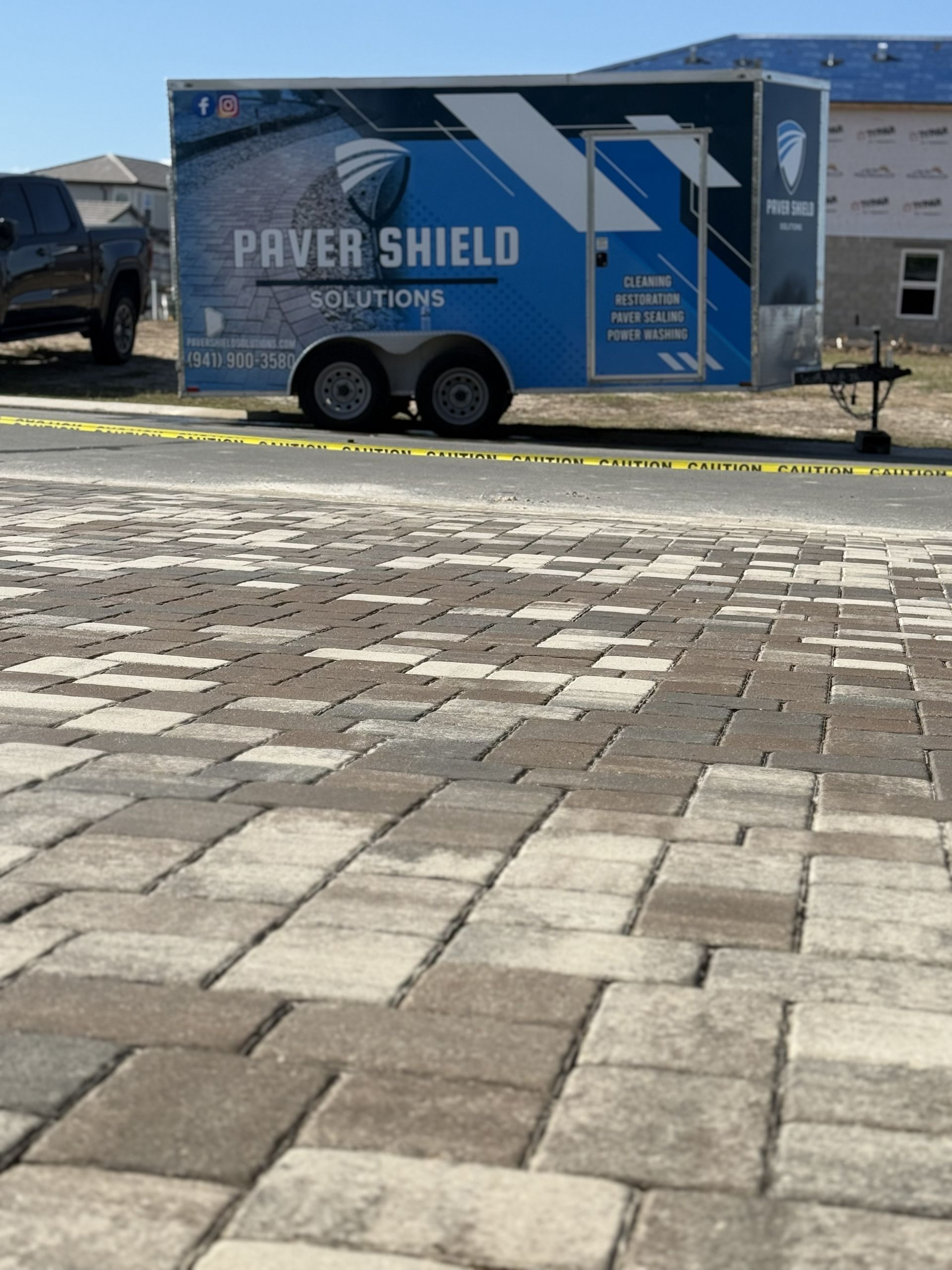 Blue and gray Praver Shield Solutions trailer parked beside a brick-paved lot under a clear sky
