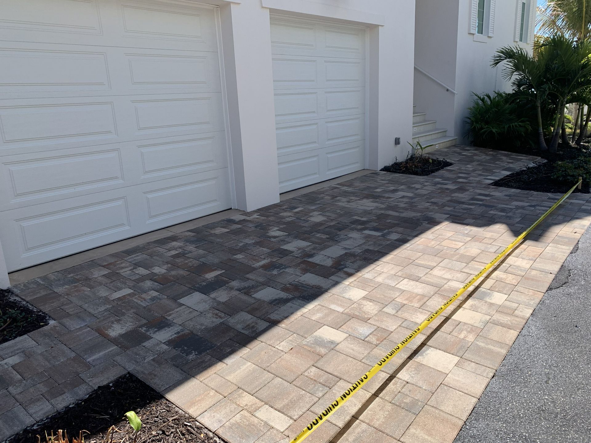 Driveway with white garage doors, brick pavers, and a yellow hose along the right edge.