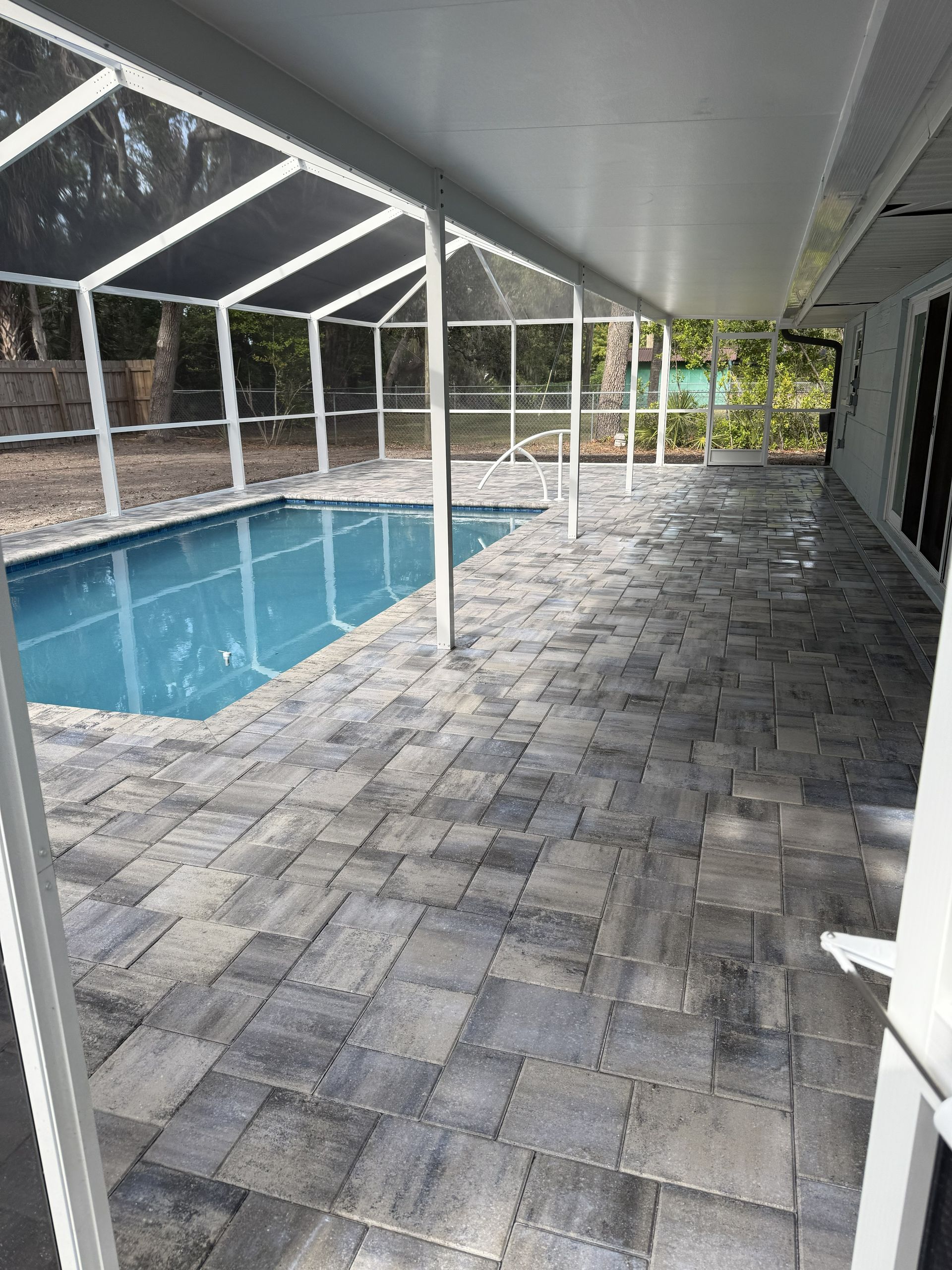 Covered pool patio with gray pavers beside a screened-in swimming pool and house exterior.